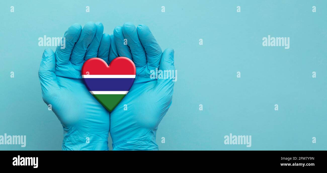 Ärzte Hände tragen chirurgische Handschuhe halten Gambia Flagge Herz Stockfoto
