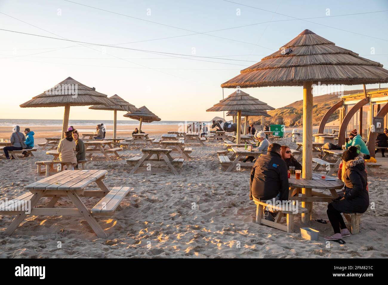 Die Leute stehen am Strand, um den Sonnenuntergang über dem Perranporth Beach in Cornwall, Großbritannien, zu beobachten Stockfoto