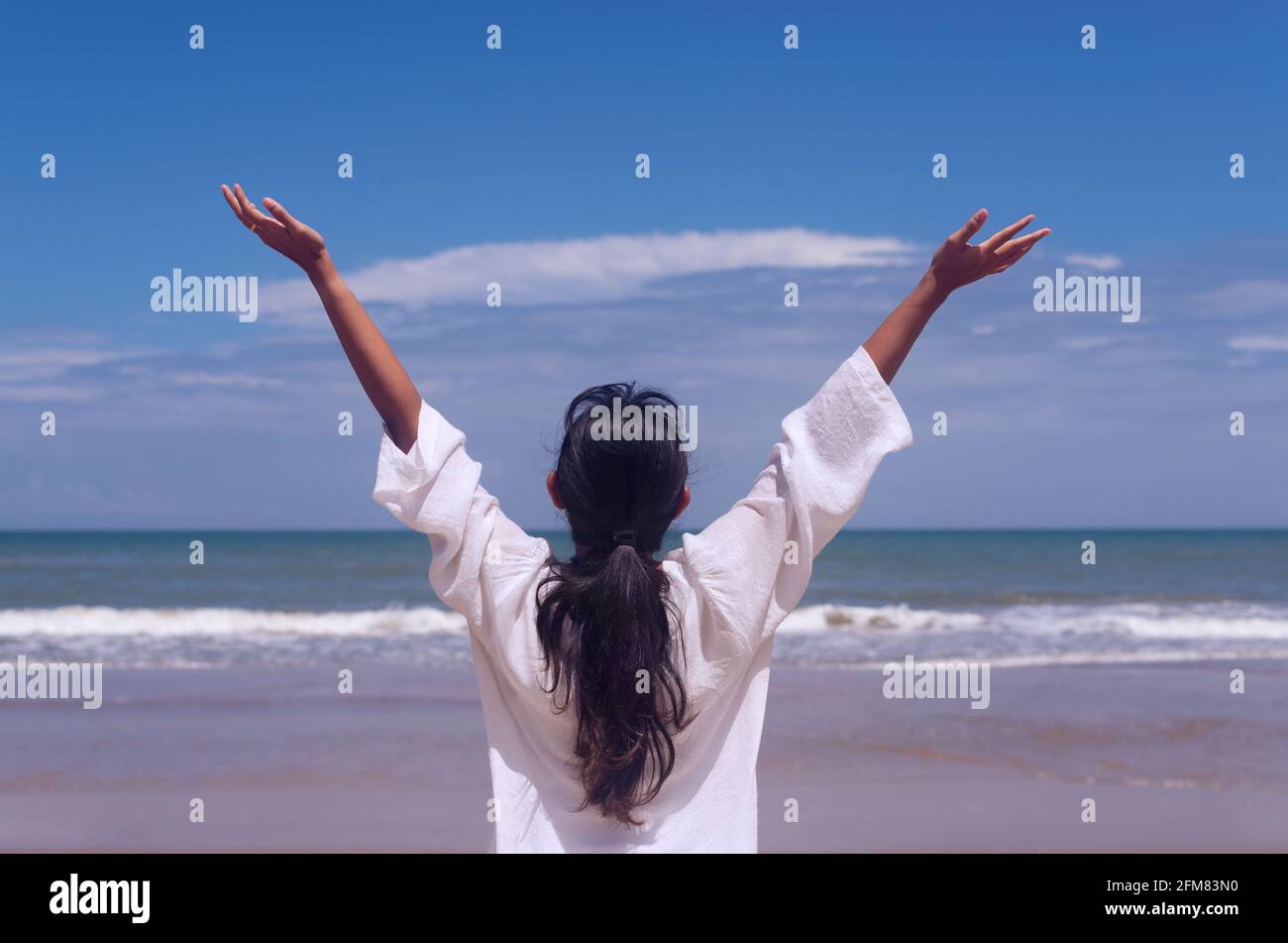 Menschen und gesundes Lifestyle-Konzept - Rückansicht junge Frau Genießen Sie den Blick auf das tropische Meer, während sich die Arme nach oben frei fühlen Mit blauem Himmel Hintergrund Stockfoto