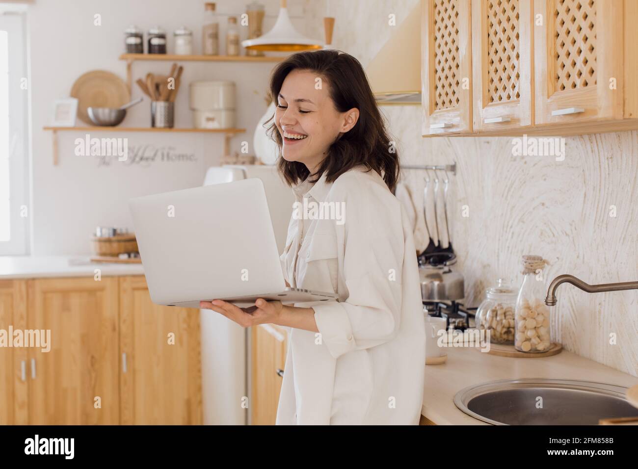 Eine lächelnde junge Frau in einer Küche, genießt ein Videogespräch, lernt sich auf einer Website kennen. Eine Frau verbringt Zeit in einem sozialen Netzwerk Stockfoto