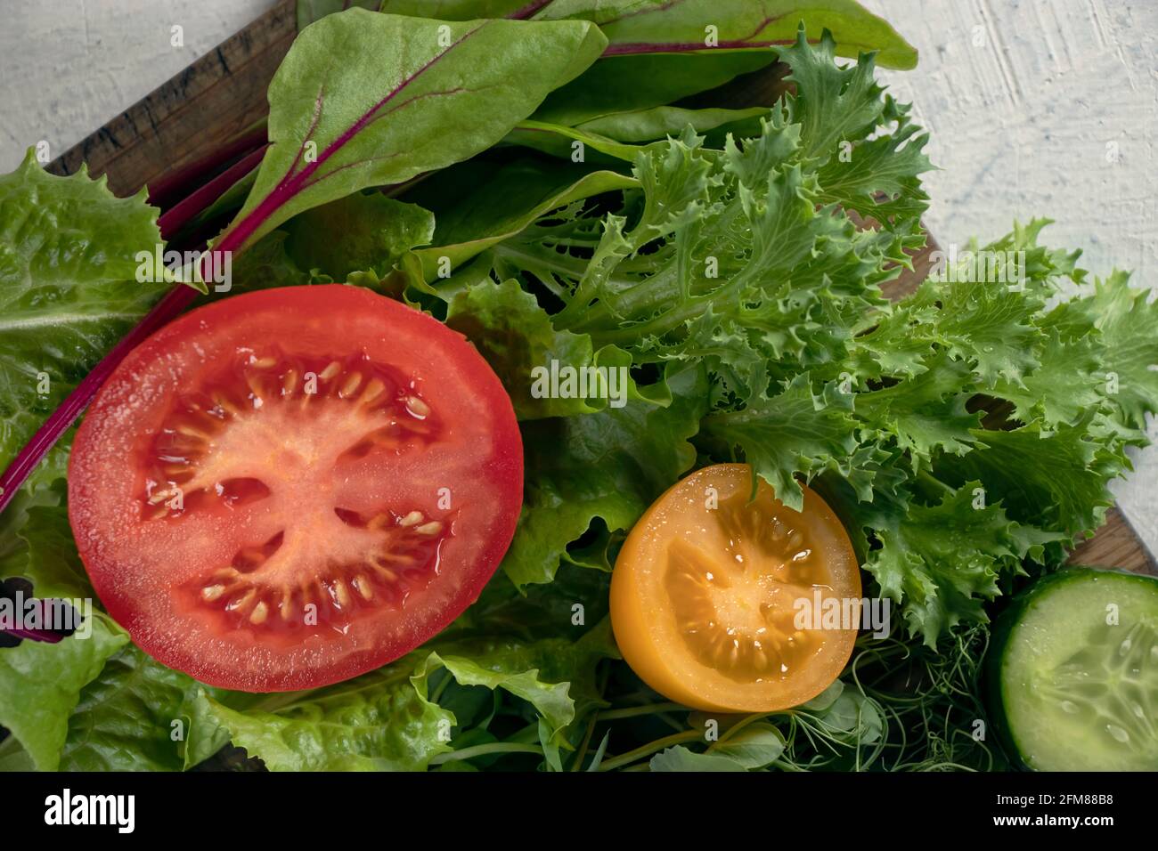Nahaufnahme verschiedener Salatsorten und Gurken, roter und gelber Tomaten auf Schneidebrett. Junge saftige Sprossen aus Erbsen oder Bohnen, Rübensprossen und gree Stockfoto