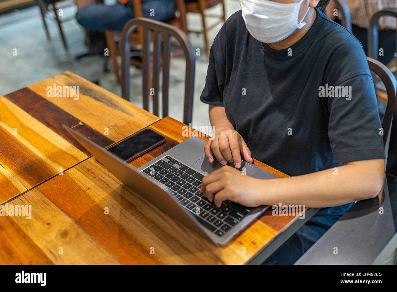 Frau mit Schutzmaske und Laptop in der Cafeteria Stockfoto
