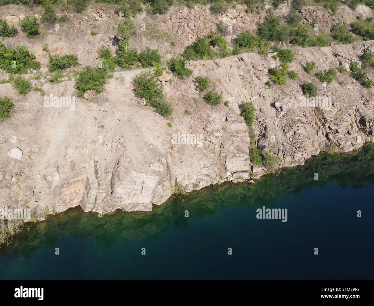 Felsige Ufer des Radon Lake an einem sonnigen Sommermorgen. Luftaufnahme eines alten überfluteten Granitsteinbruchs. Ein malerischer Teich. Stockfoto