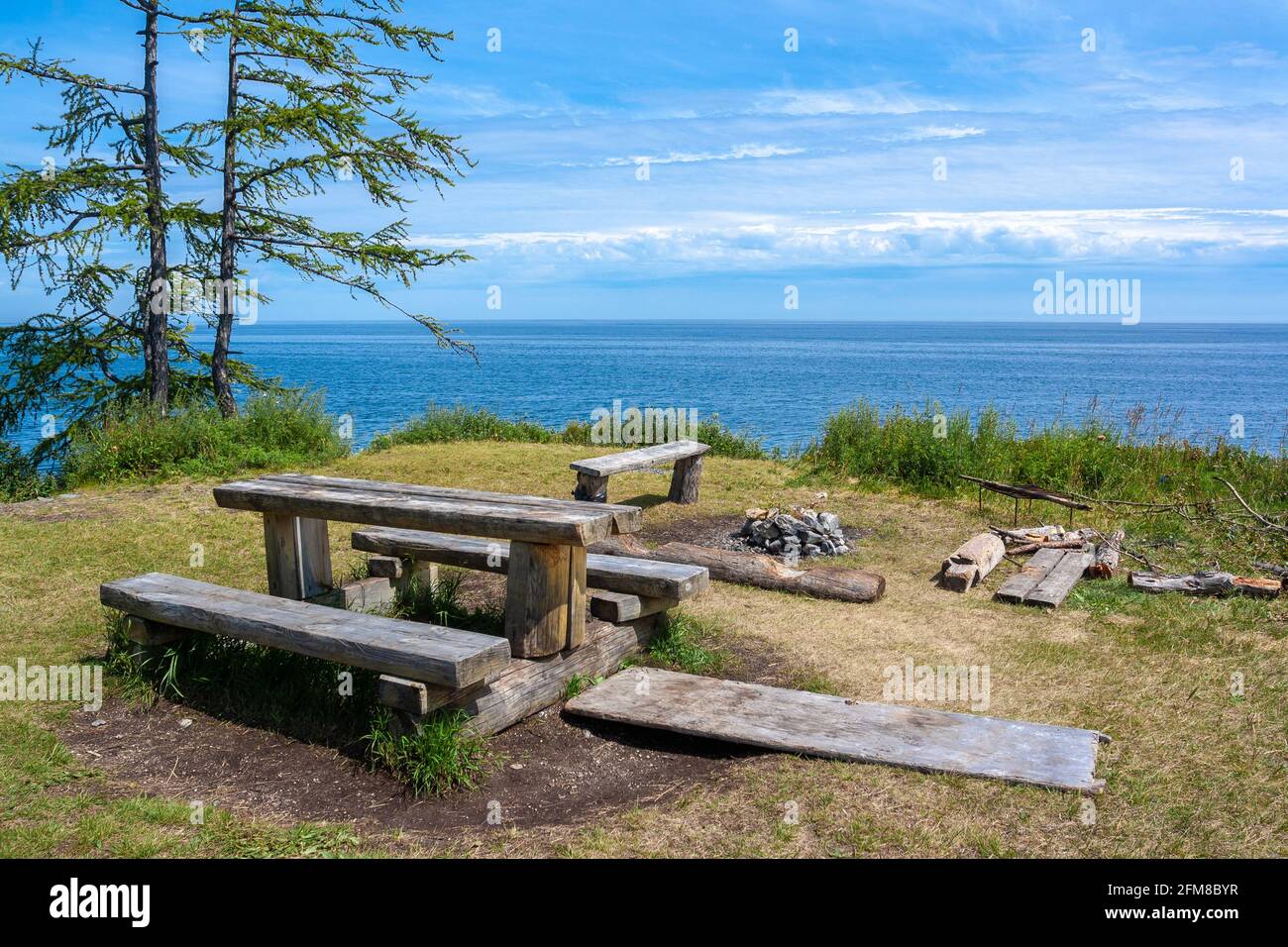 Wanderruheplatz mit Bänken, Tisch und Lagerfeuerplatz am Baikalsee. Blauer Himmel mit Wolken und Sommersonne. Stockfoto