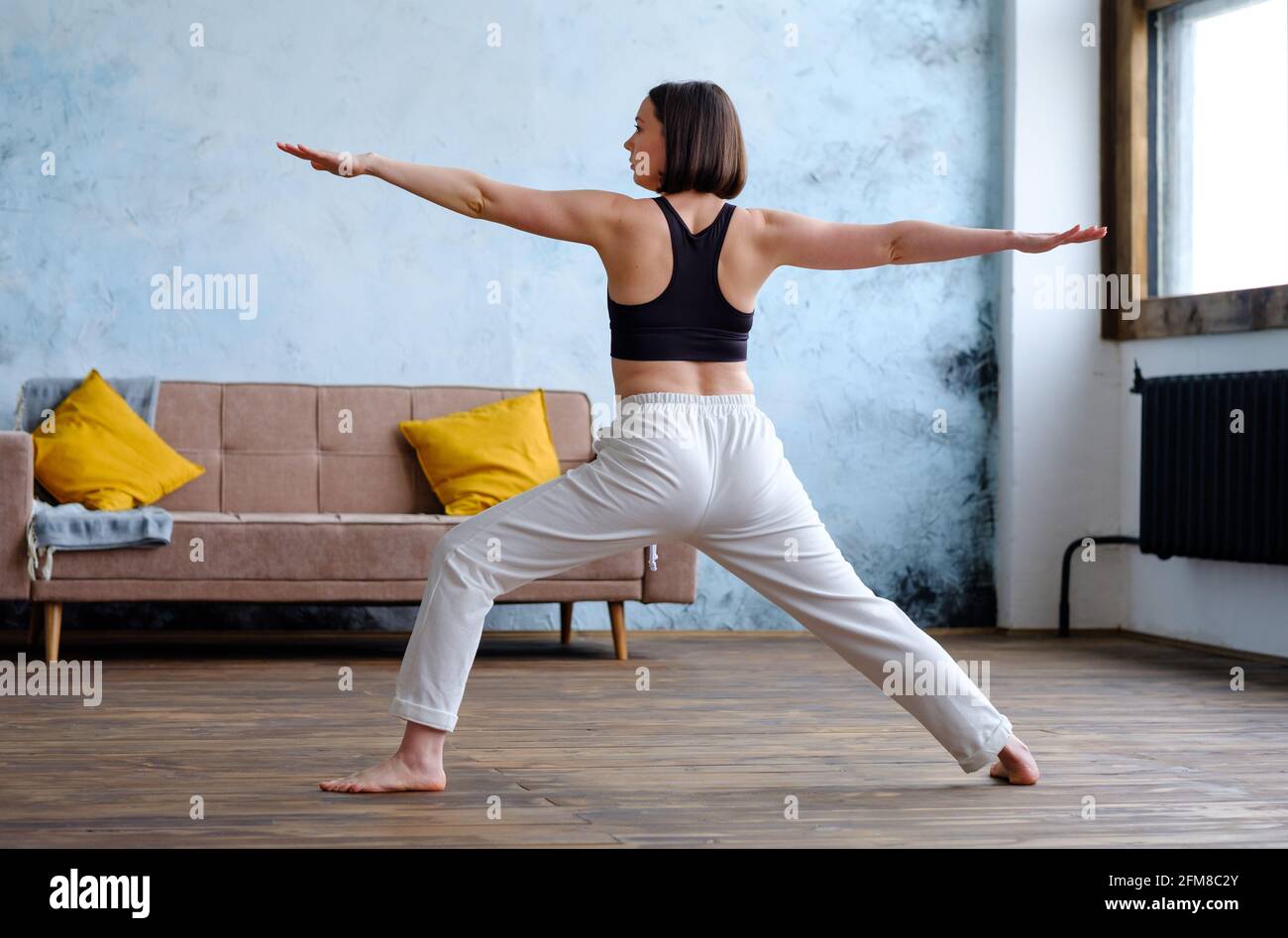 Frau in ihrem Wohnzimmer in Krieger-Yoga-Pose. Stockfoto