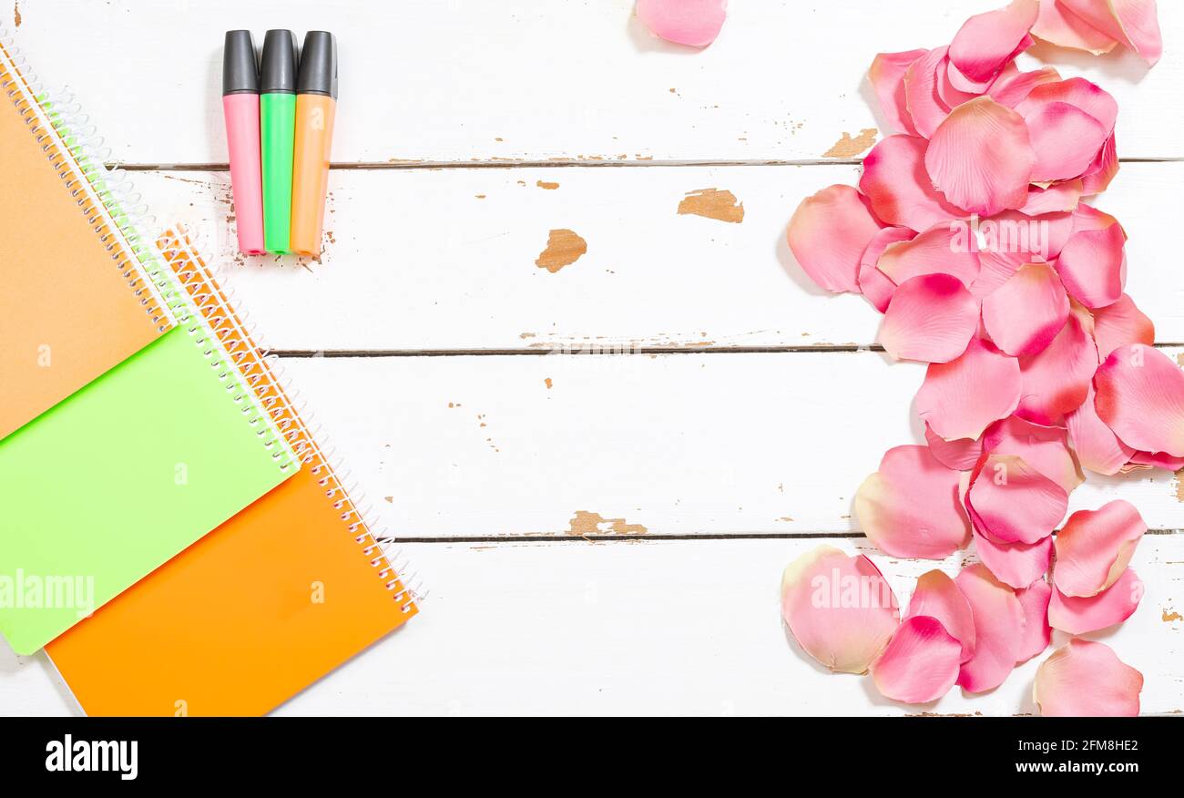 Foto von farbigen Leuchtstofflampen und verschiedenen Notizbüchern auf einem Holzhintergrund weiß und geschmückt mit Rosenblättern.das Foto ist Eine Aufnahme über dem Kopf mit Stockfoto