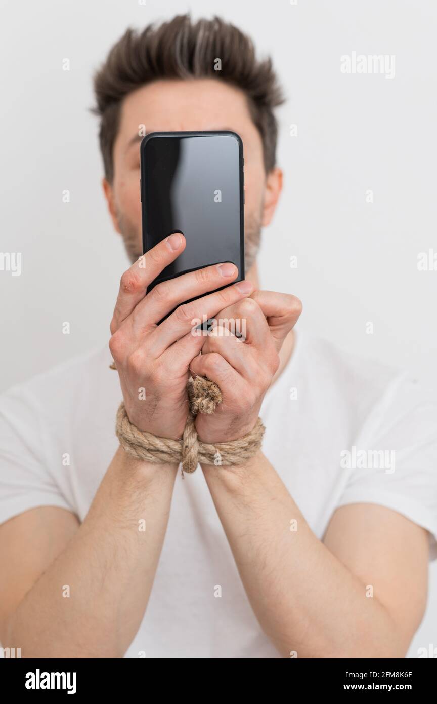 Eine Person mit gefesselten Händen, die ein Smartphone, eine Internetabhängigkeit oder eine sucht in sozialen Medien hält. Stockfoto