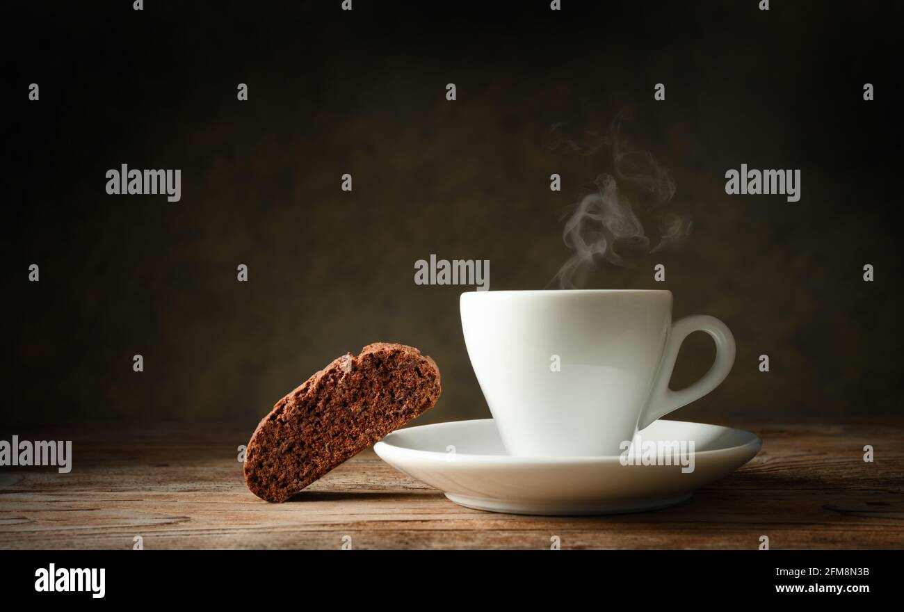 Einsame Kaffeepause. Schokoladenkeks und dampfender Espresso-Becher in dunkler Einstellung, Platz für Text. Stockfoto