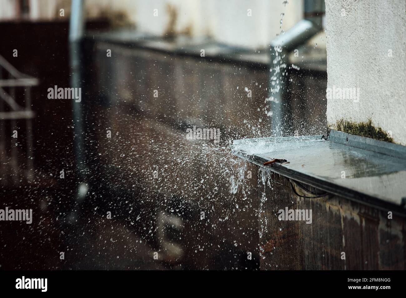 Fallende Regentropfen brechen auf der Kante. Spritzer aus fließendem Wasser. Drainpipe vom Dach eines Gebäudes während eines Regensturms Stockfoto