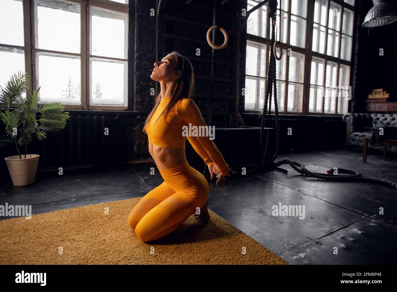 Junge Yogi-Frau, die Yoga-Konzept praktiziert, eine einbeinige King Pigeon-Übung macht, trainiert, Sportkleidung trägt, Loft-Studio Hintergrund Stockfoto