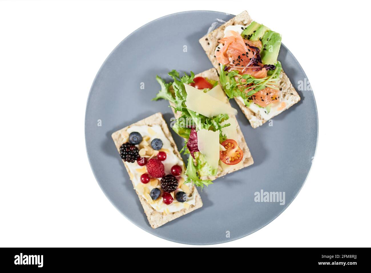 Draufsicht Nahaufnahme von drei Diätbroten mit Lachs, Avocado, Grüngemüse, Tomaten und frischen Beeren auf weißem Hintergrund. Konzept von leckeren Snacks mit Meeresfrüchten im Restaurant oder zu Hause. Stockfoto