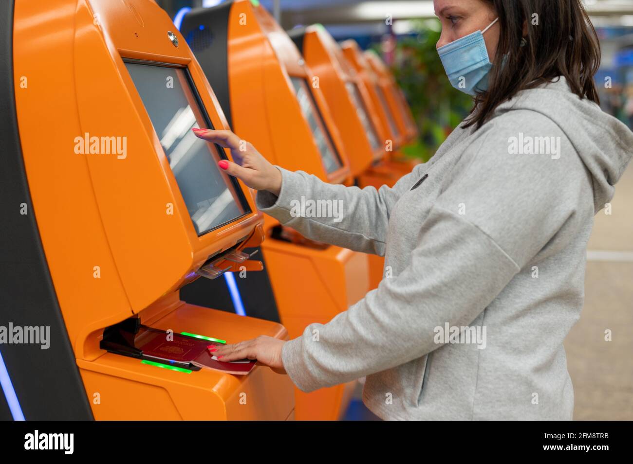 Frau mit Schutzmaske gegen Coronavirus, die mit dem Flugzeug reist und mit einem Automaten am Flughafen eincheckt. Bestätigen Sie die Flugdetails Stockfoto