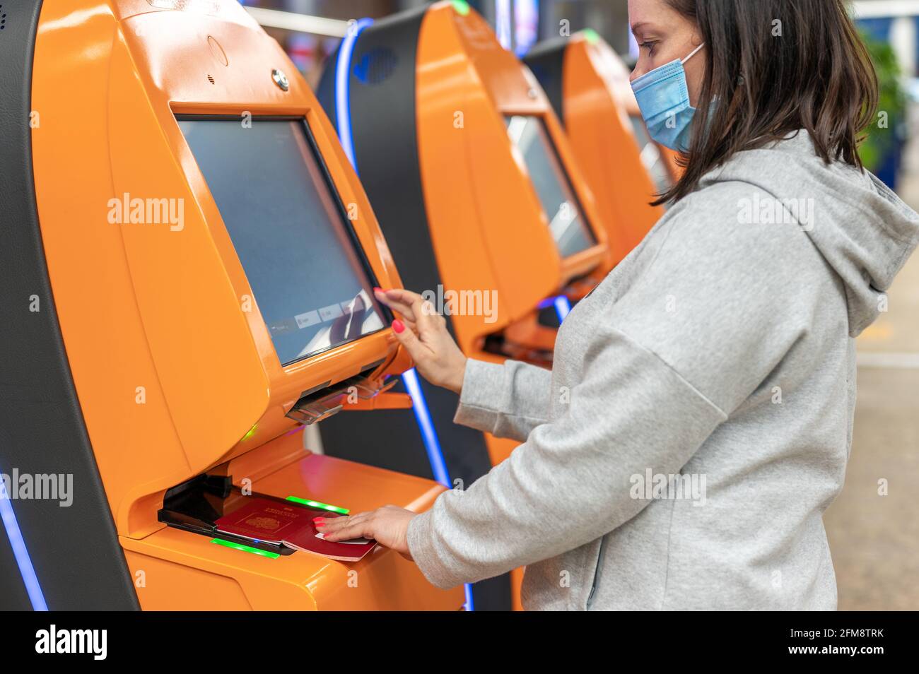 Frau mit Schutzmaske gegen Coronavirus, die mit dem Flugzeug reist und mit einem Automaten am Flughafen eincheckt. Selbstbedienungsmaschine A Stockfoto
