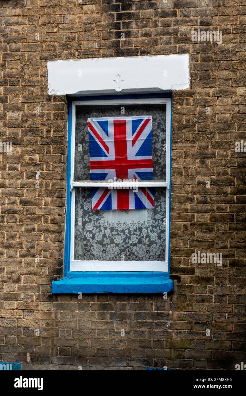 In einem Schiebefenster mit einem Netzvorhang in einer Backsteinmauer wird die Unionsflagge dargestellt. Cambridge, Großbritannien Stockfoto