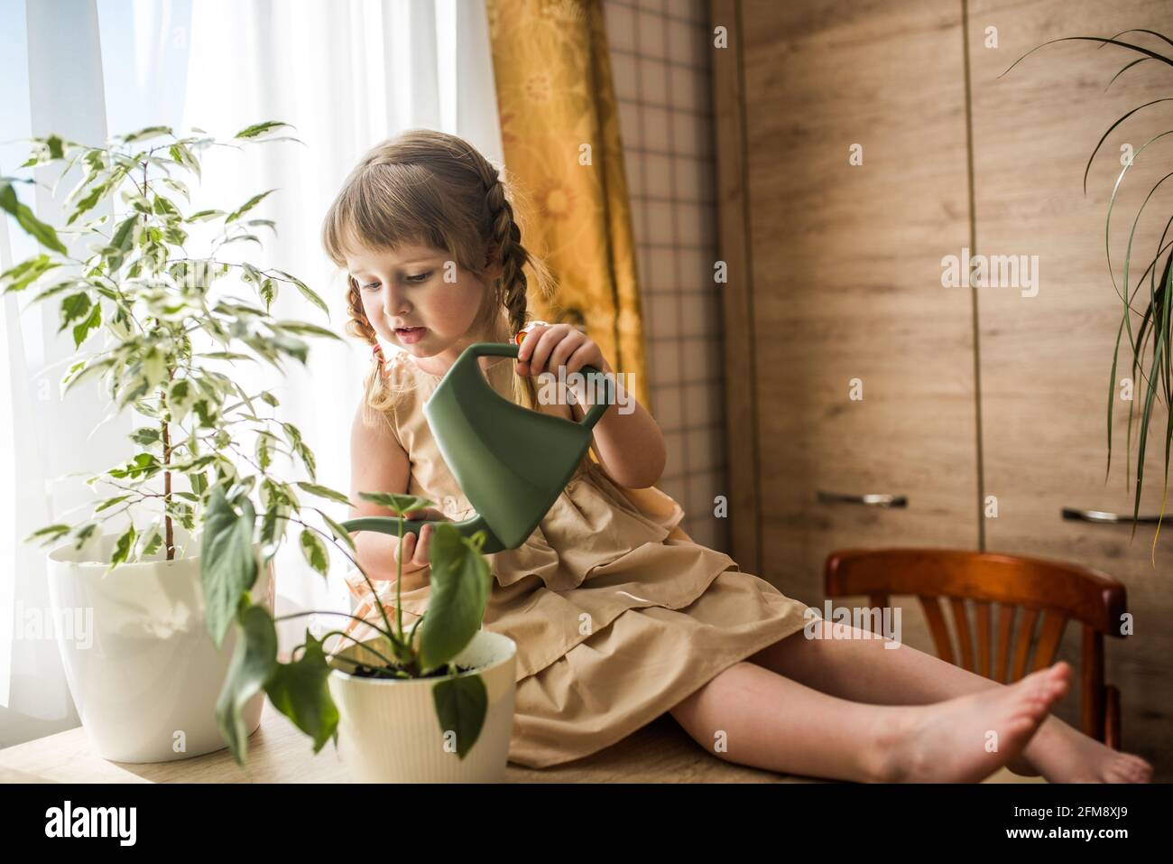 Happy kleine niedliche Baby Mädchen kümmert sich um Zimmerpflanzen. Mädchen Bewässerung und Spritzen Zimmerpflanzen zu Hause Stockfoto