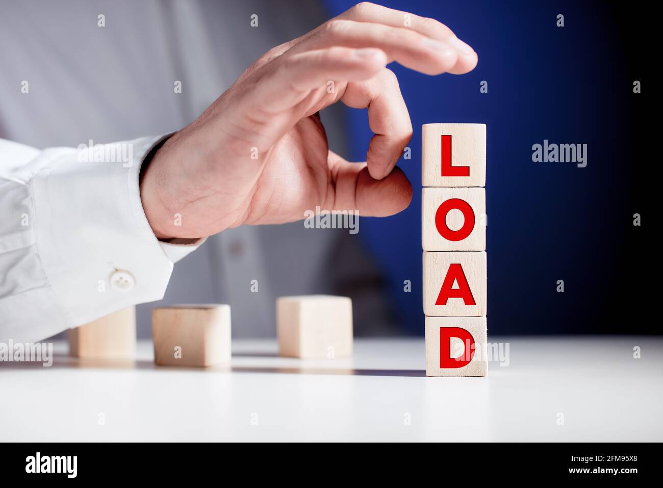 Das Wort load, das mit einer Geschäftsmannes-Hand auf gestufte Holzwürfel geschrieben wurde, ist dabei, die Würfel zu kippen. Überlastung, Überlastung und Entladung im Geschäft oder bei der Arbeit Stockfoto