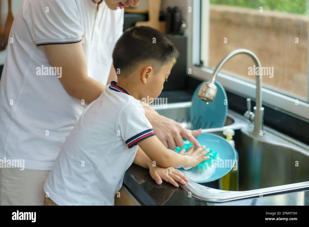 Asiatischer Vater lehrt seinen Sohn, wie man Geschirr waschen, Hilfe bei der Hausarbeit in der Küche zu Hause, Väter interagieren mit ihren Kindern während der d Stockfoto