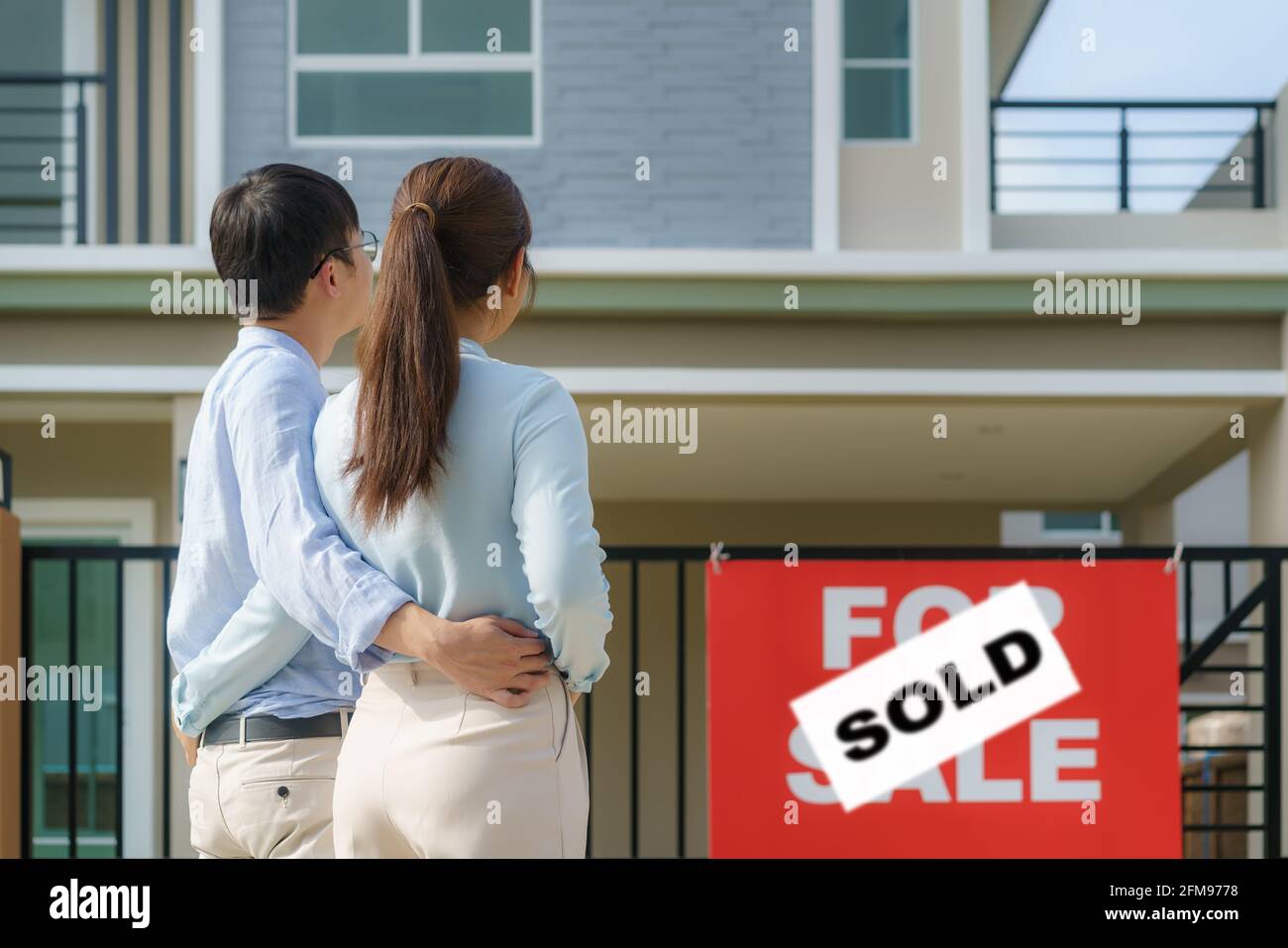 Hinteres Porträt des jungen asiatischen Paares, das zusammen steht und umarmt und vor ihrem neuen Haus glücklich aussieht, um neues Leben zu beginnen. Familie, Alter, Zuhause, echt Stockfoto