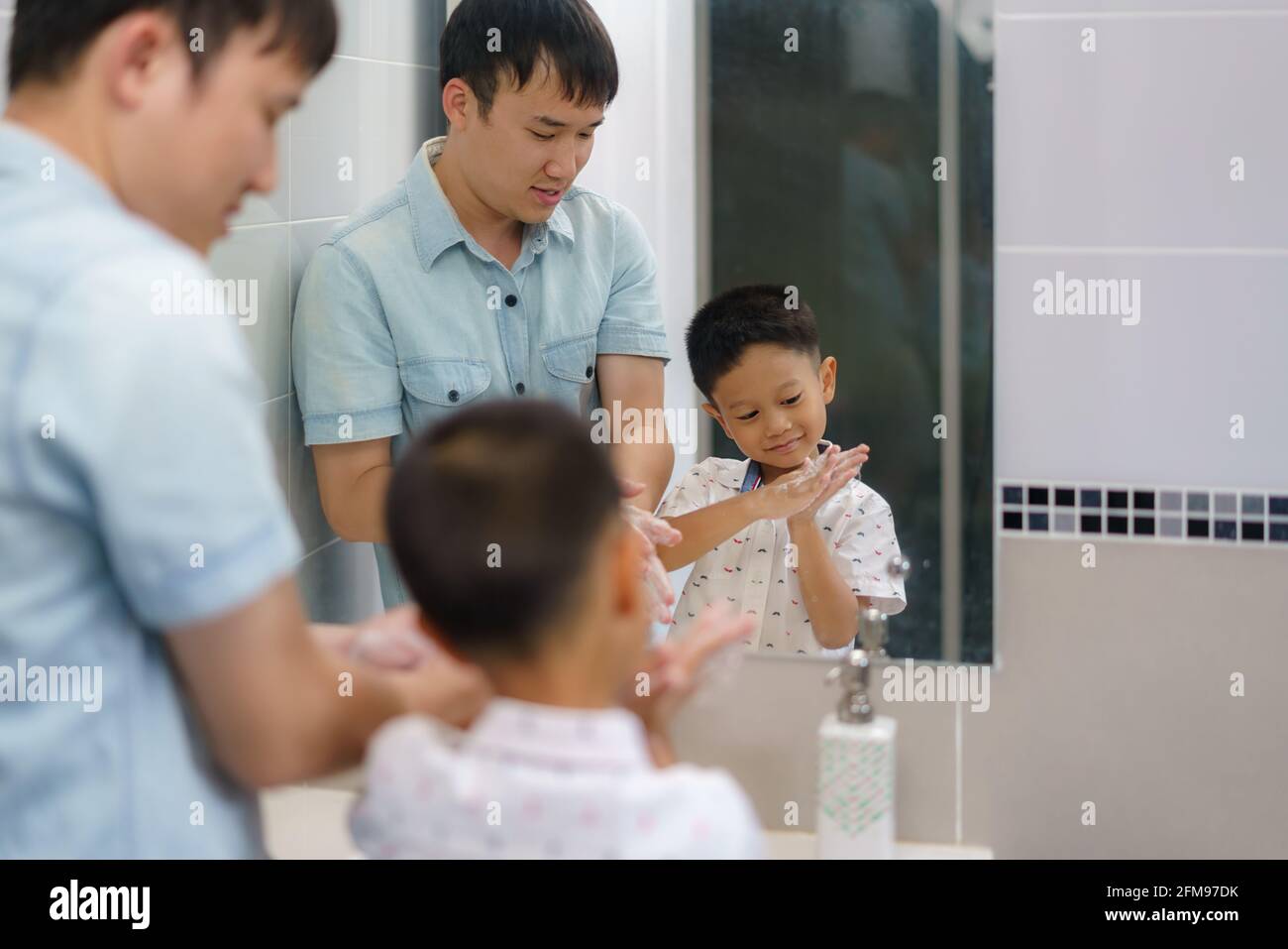 Der asiatische Vater lehrt seinen Sohn, sich im Badezimmer die Hand selbst zu waschen, Väter interagieren den ganzen Tag über mit ihren Kindern. Stockfoto
