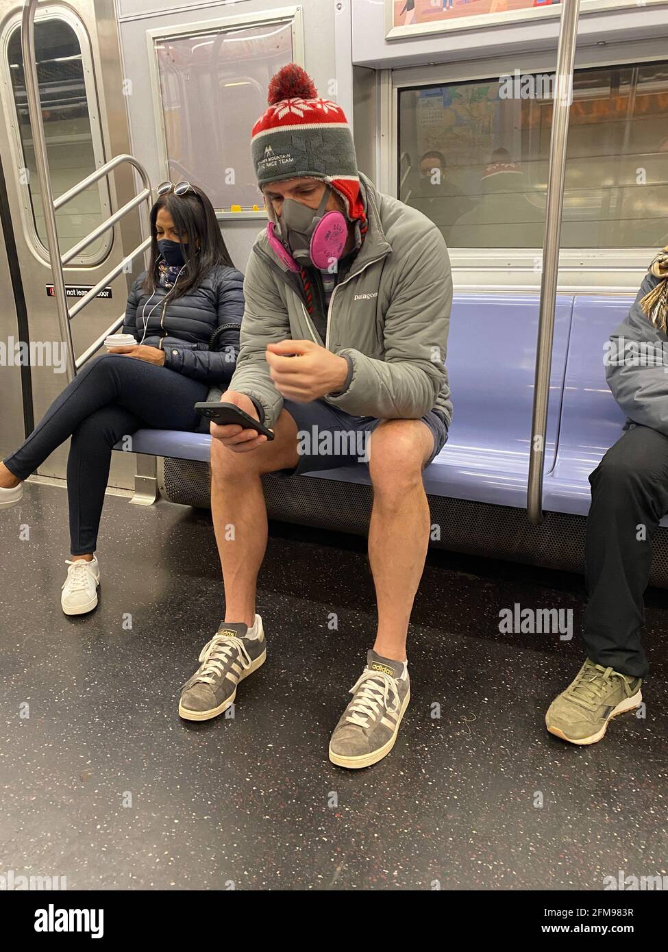 Während der Pandemie von Covid-19 in New York City trägt der Mann eine sehr ernst aussehende Gesichtsmaske in einem U-Bahn-Zug. Stockfoto