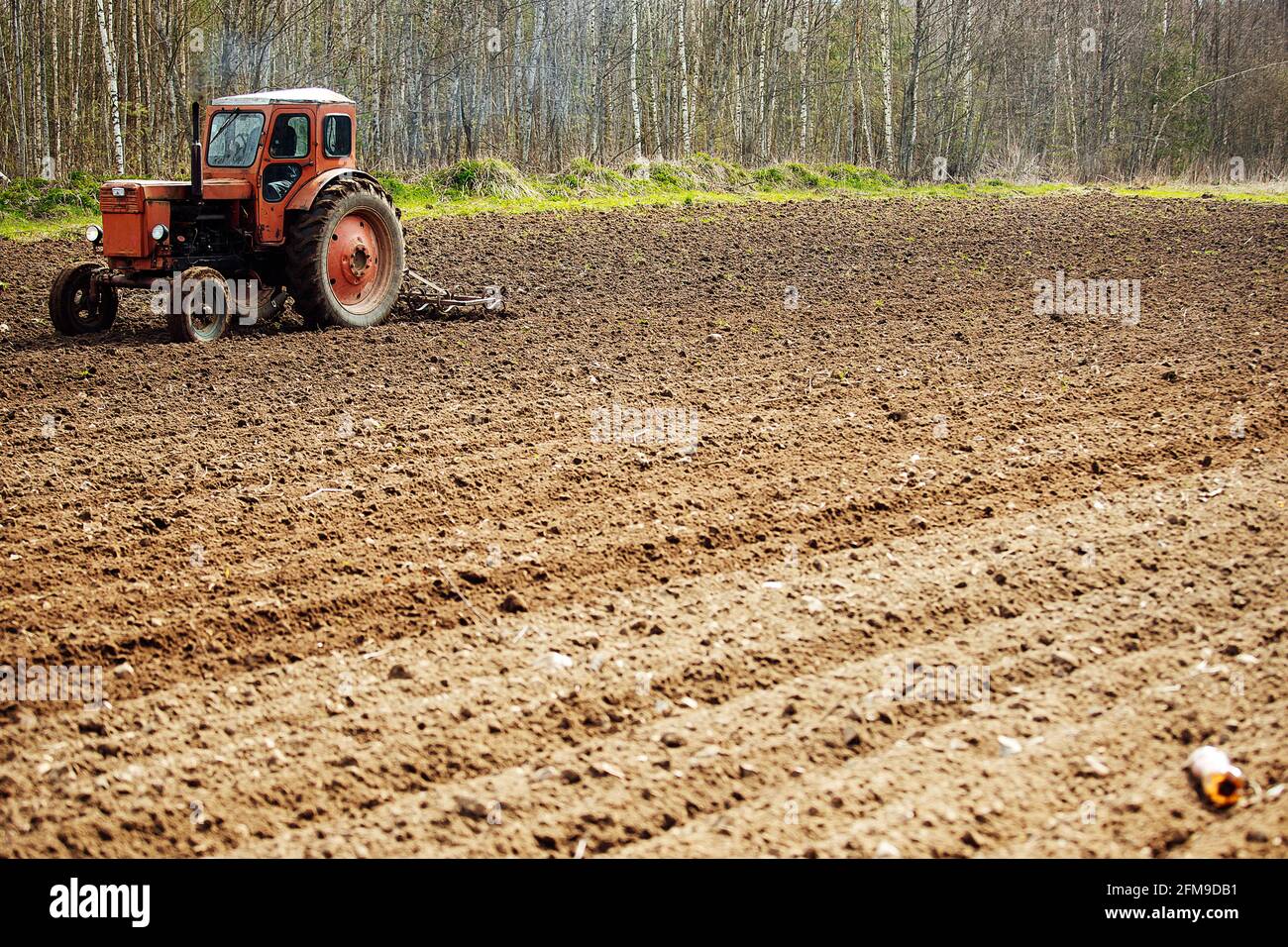 Ein Traktor pflügt ein Feld. Vorbereitung der landwirtschaftlichen Flächen für die Pflanzung. Ein mechanischer Pflug macht Furchen im Boden. Anbau von fruchtbarem Land Stockfoto