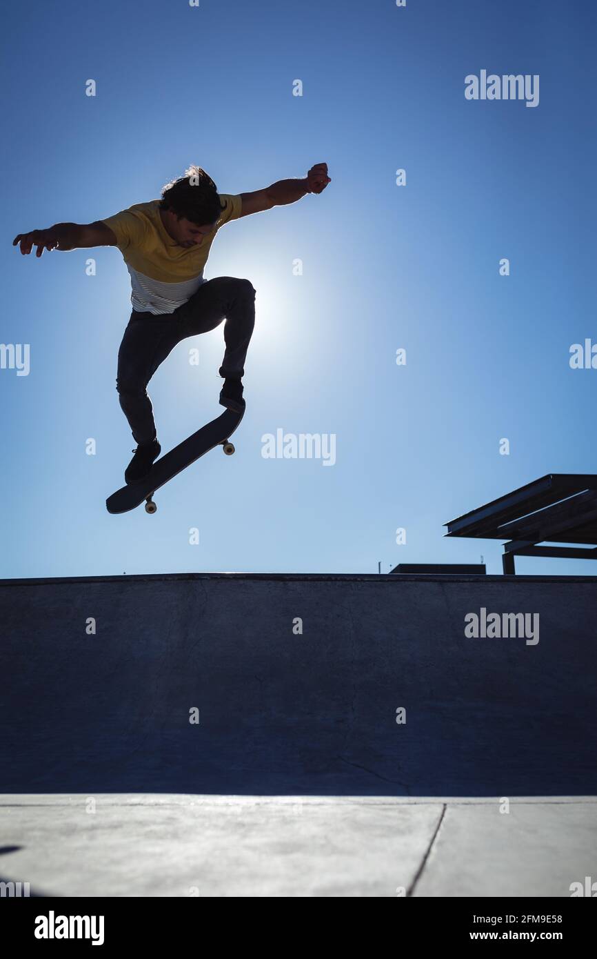 Kaukasischer Mann springt und Skateboarding an sonnigen Tagen Stockfoto