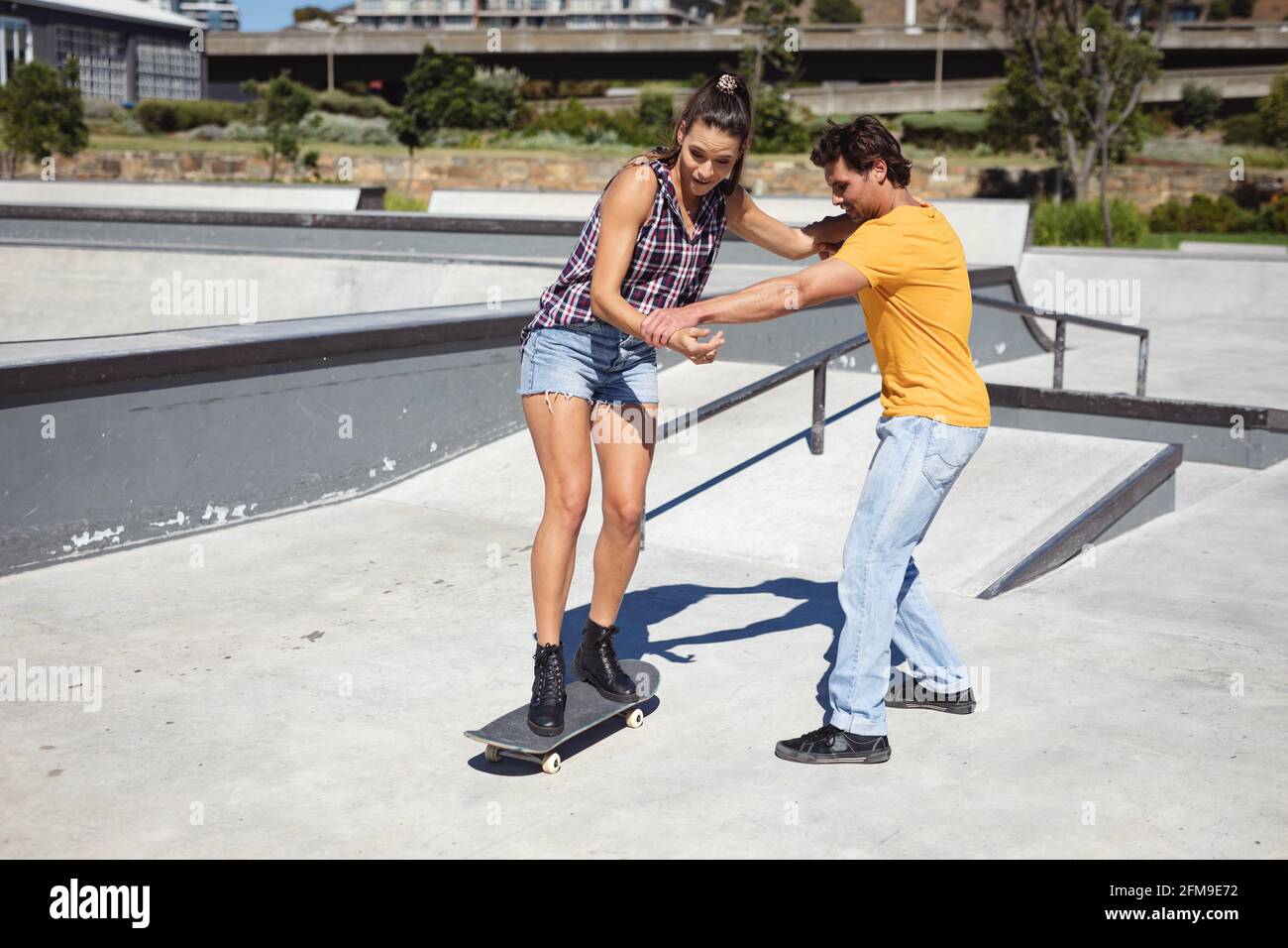 Kaukasischer Mann lehrt Frau, wie man Skateboard an sonnigen Tag Stockfoto