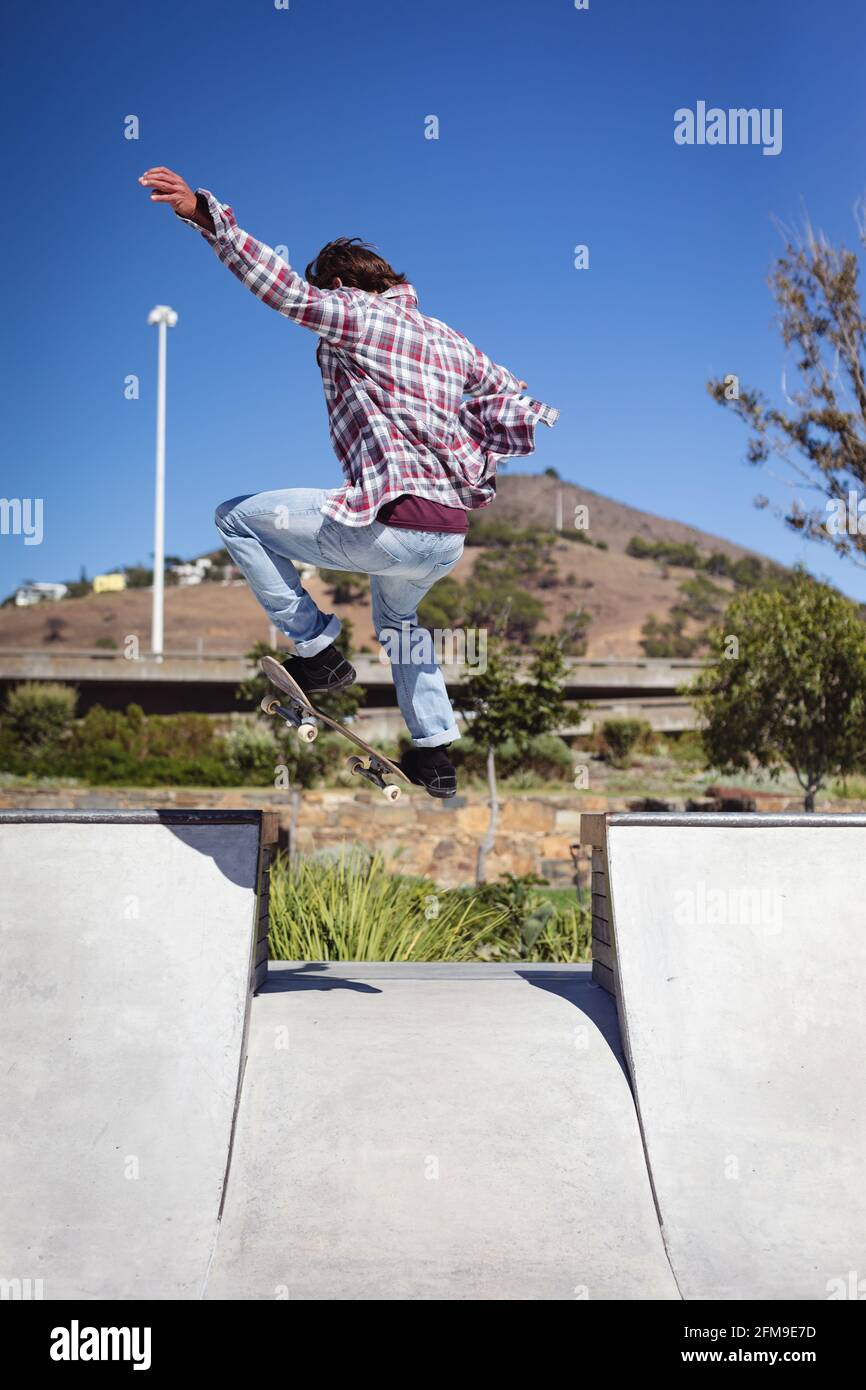 Rückansicht des kaukasischen Mannes beim Springen und Skateboarden bei Sunny Tag Stockfoto