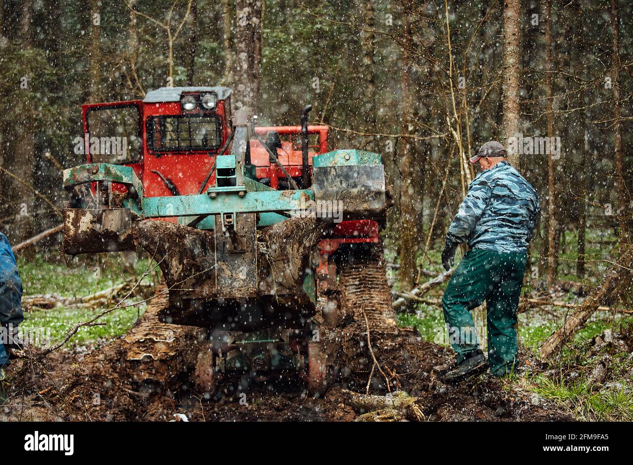 Ein Raupentraktor fährt durch eine Waldlichtung. Ein industrieller Bulldozer steckt im Schlamm fest. Lastwagen laufen im Boden Stockfoto
