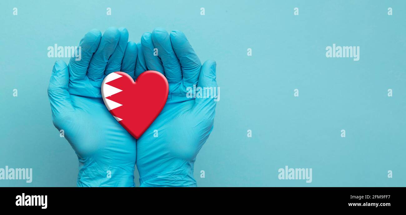 Ärzte Hände tragen chirurgische Handschuhe, die das Herz der Bahrain Flagge halten Stockfoto