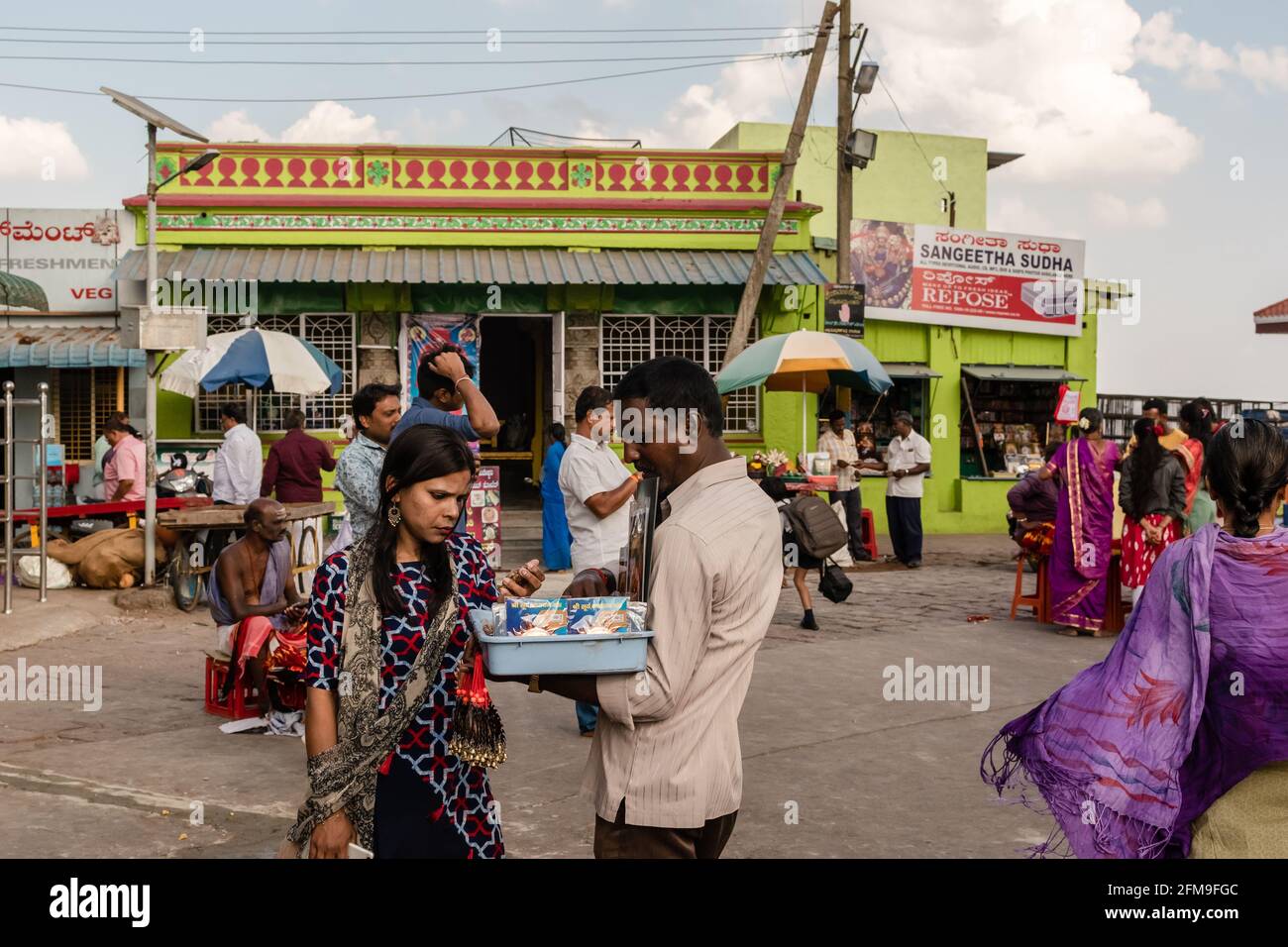 Mysuru, Karnataka, Indien - 2019. Januar: Ein indischer Straßenhändler, der vor dem alten Chamundeshwari-Tempel in Chamu religiöse Gegenstände an eine Frau verkauft Stockfoto