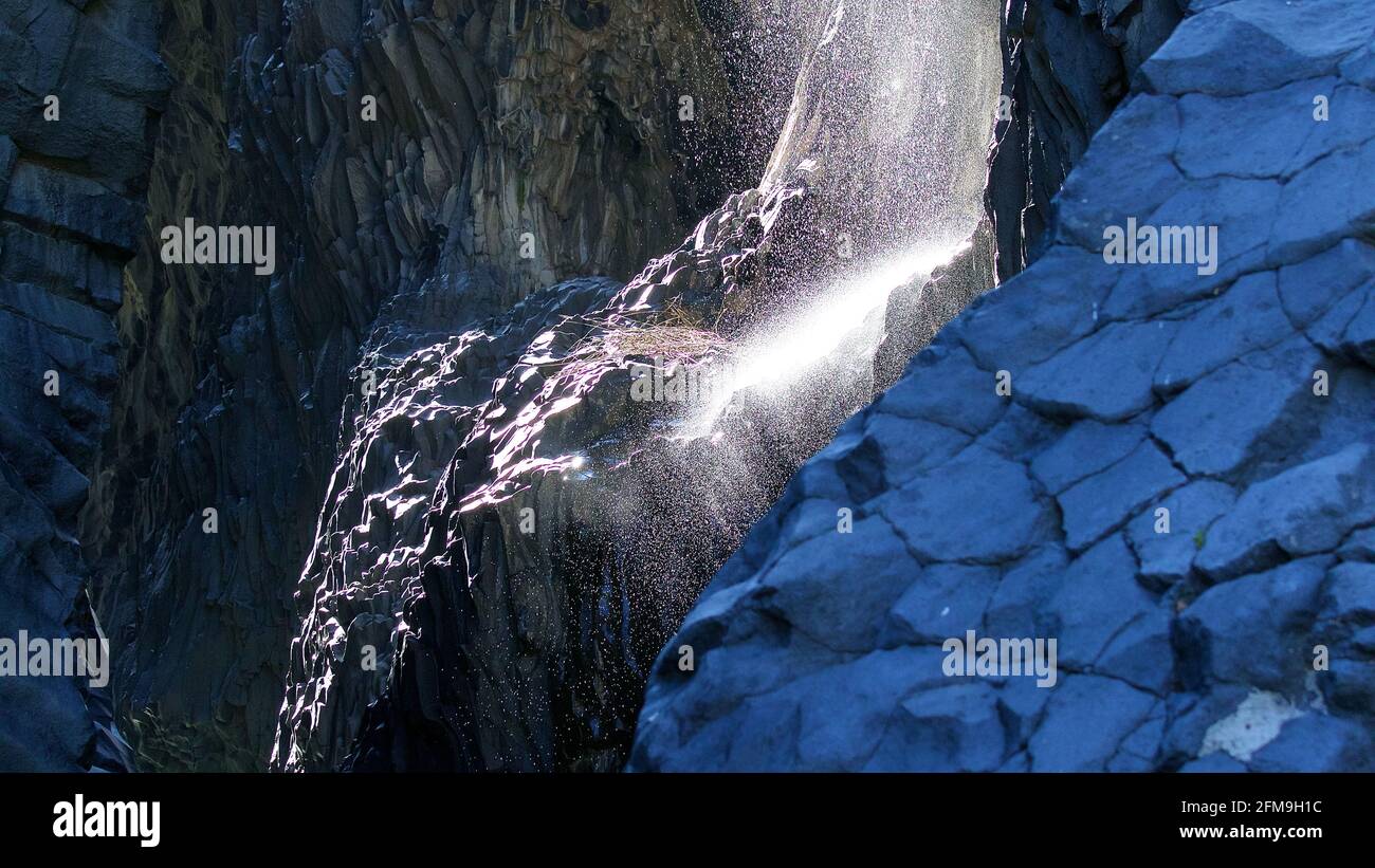 Italien, Sizilien, Alcantara, Alcantara-Schlucht, Fluss, Wasserfall, Wasser fällt auf einen Felsvorsprung in der Schlucht, Wasser spritzt als Spray auf, Rücklicht, bläuliche Felswände Stockfoto