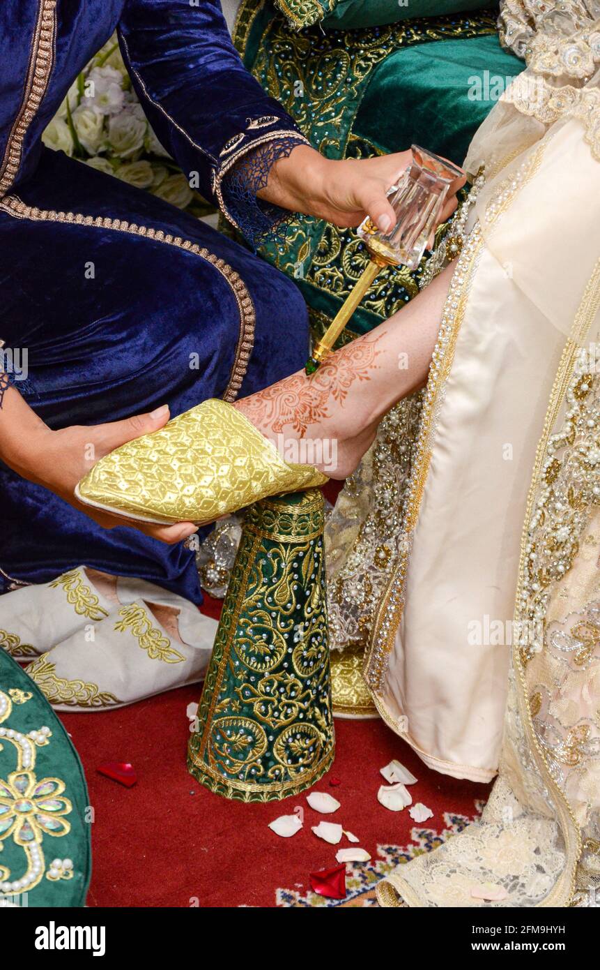 Marokkanische Hochzeit. Tradition der Henna-Nacht im arabischen Maghreb. Ein Mädchen, das versucht, die Braut in traditionellen marokkanischen Schuhen zu kleiden Stockfoto