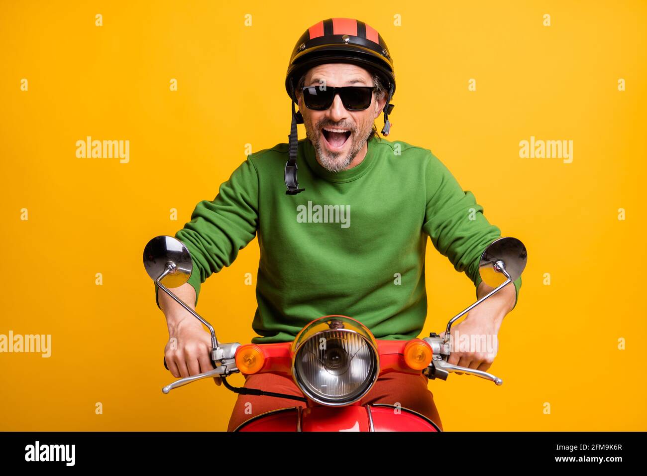 Foto von stauned lustigen Kerl Fahrt Moped tragen Helm Brille Grüner  Pullover isolierter gelber Hintergrund Stockfotografie - Alamy