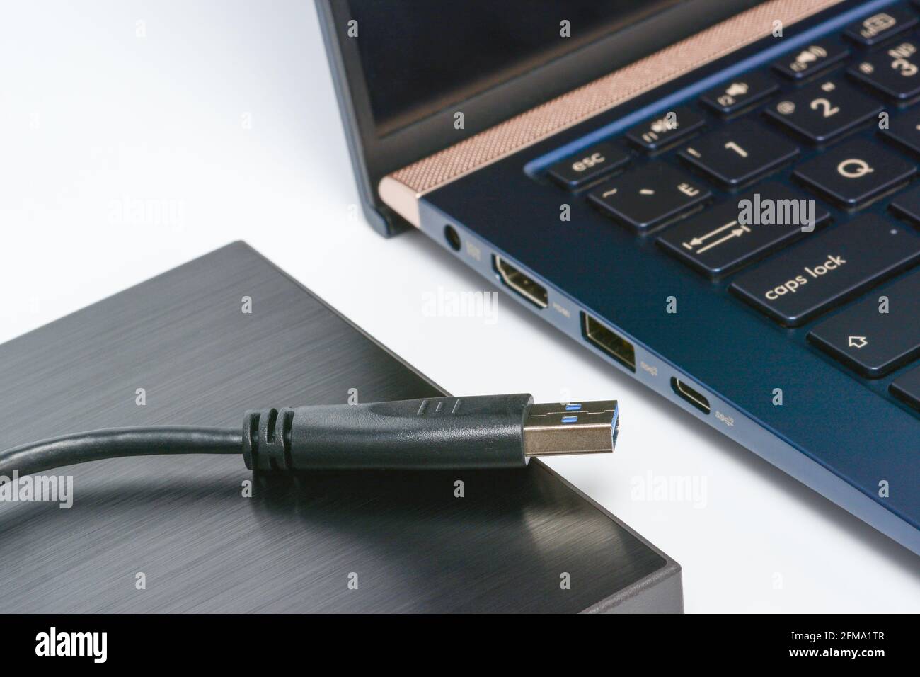 Externe Festplatte mit USB 3.0-Kabel und Laptop in der Nähe. Konzept der Datenspeicherung auf einer tragbaren festplatte. Nahaufnahme auf weißer Oberfläche mit Schatten. Stockfoto