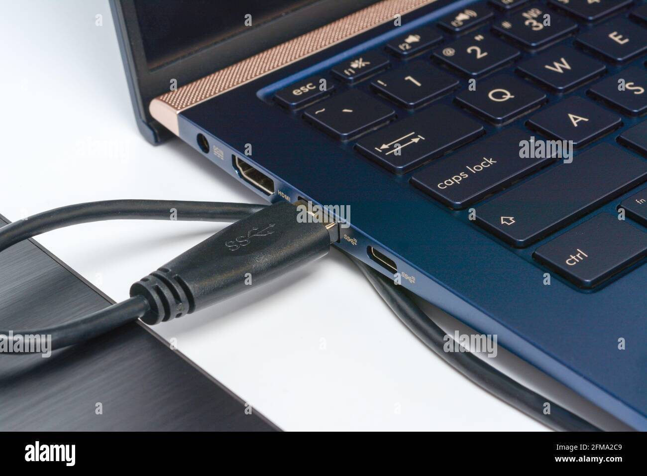 Externe Festplatte, die über ein usb 3.0-Kabel mit dem Laptop verbunden ist. Konzept der Datenspeicherung auf einer tragbaren festplatte. Nahaufnahme auf weißer Oberfläche mit Schatten. Stockfoto