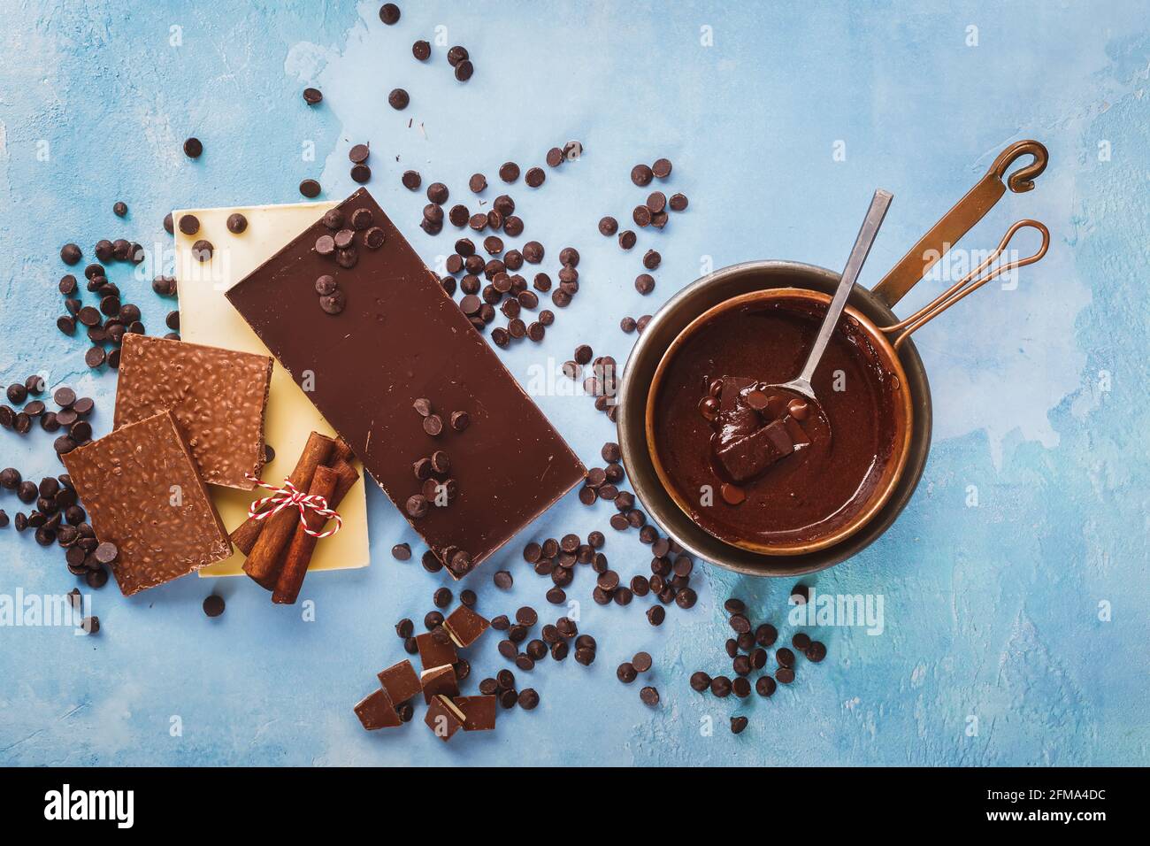 Geschmolzene Schokolade in Kupferpfanne und Tafeln aus dunkler und weißer Schokolade daneben auf rustikaler blauer Oberfläche. Draufsicht, Leerraum Stockfoto