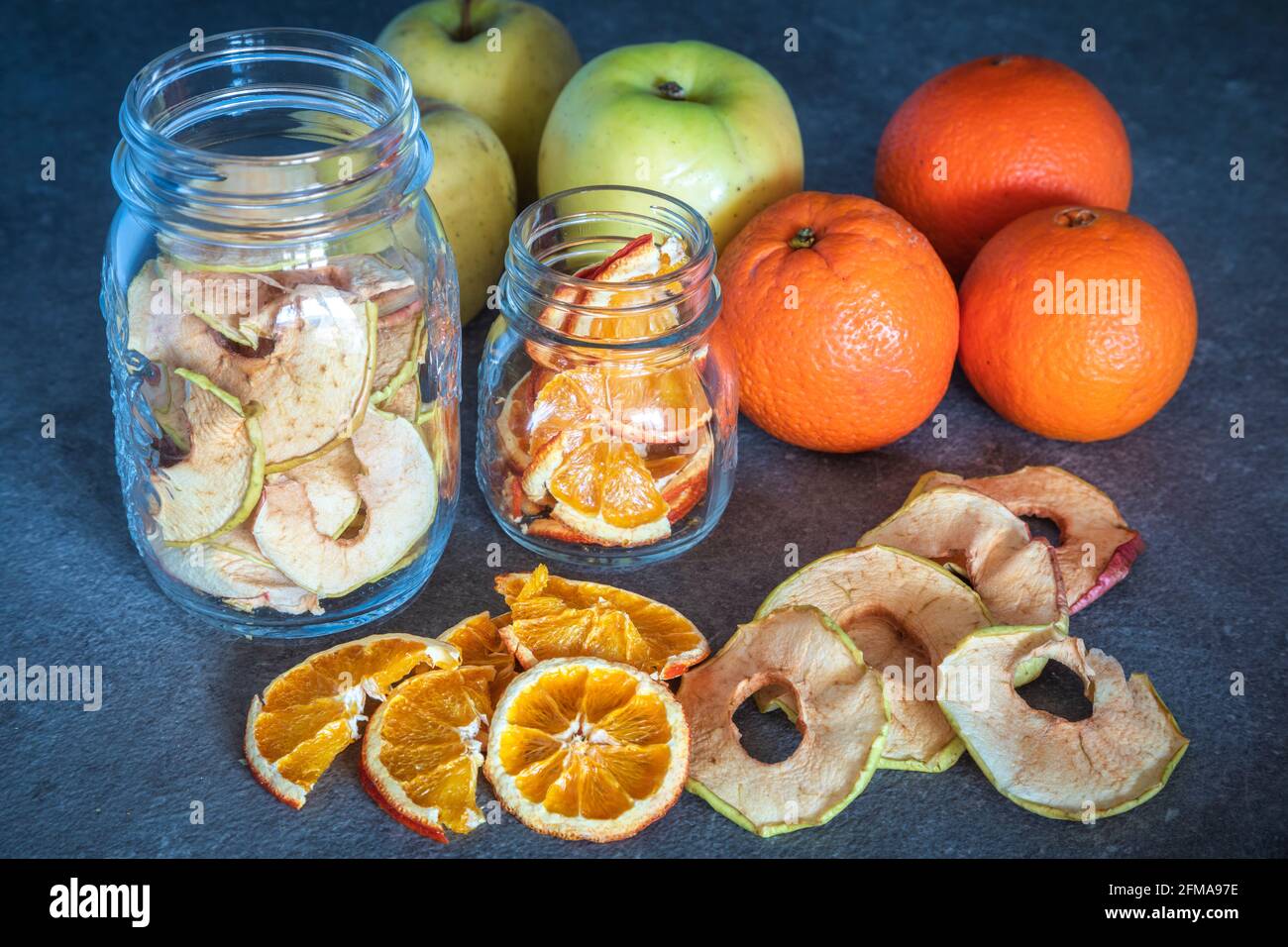 Frische Obstäpfel und Orangen sowie Apfel- und Orangenscheiben dehydriert und in Glasbehältern gelagert, hausgemachte Zubereitungen, Stockfoto
