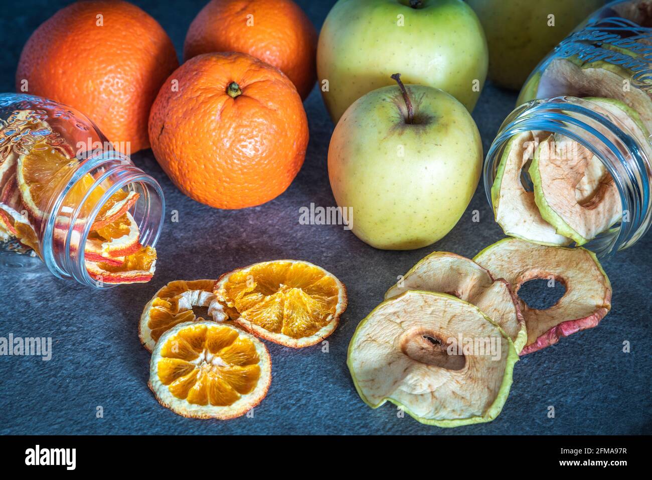 Frische Obstäpfel und Orangen sowie Apfel- und Orangenscheiben dehydriert und in Glasbehältern gelagert, hausgemachte Zubereitungen, Stockfoto