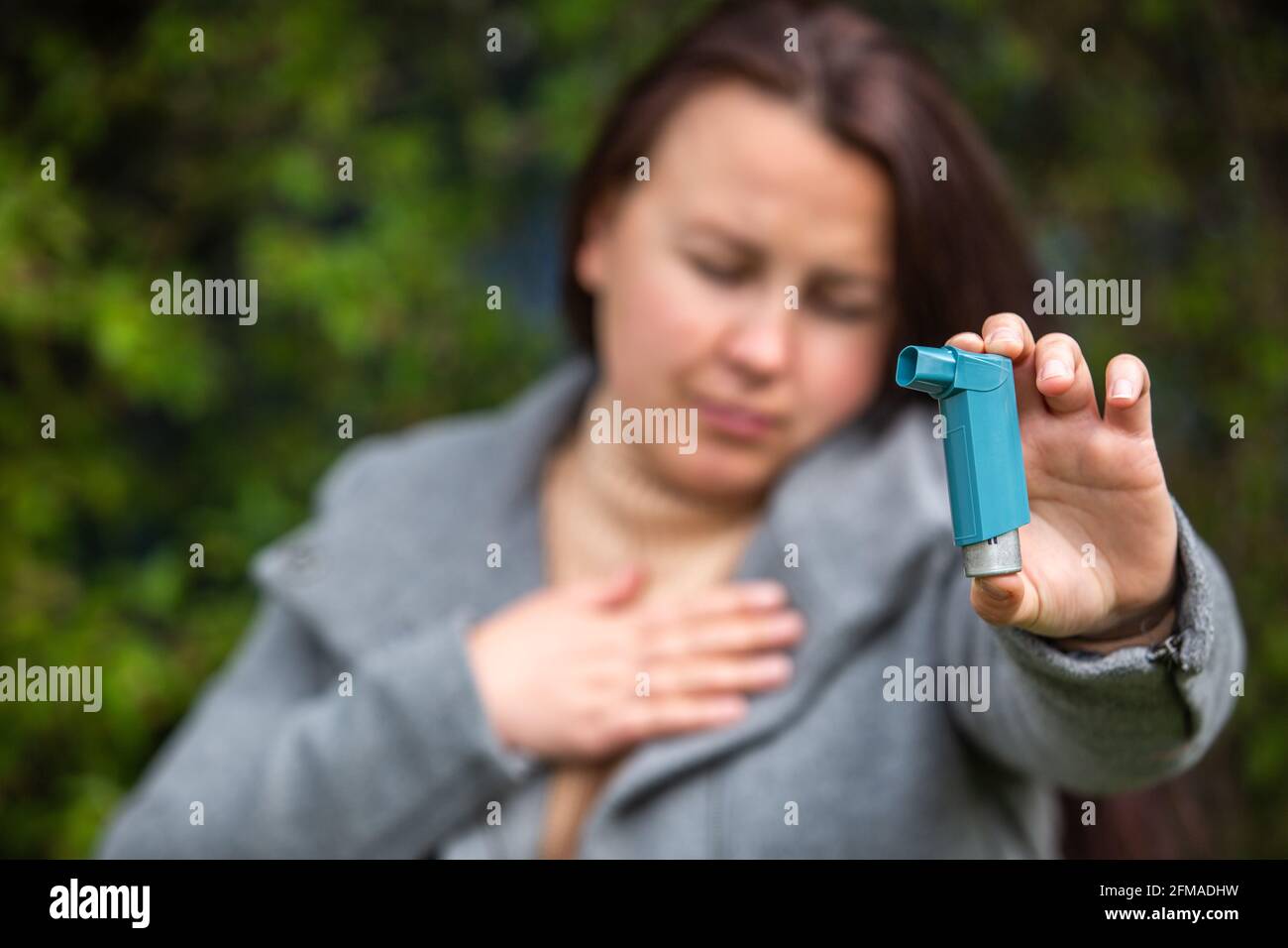 Ziemlich junge Brünette Frau mit Asthma-Angriff. Sie hält einen Inhalator. Asthmatische Frau, die einen Asthma-Inhalator während Asthmaanfällen verwendet, Gesundheitswesen Stockfoto
