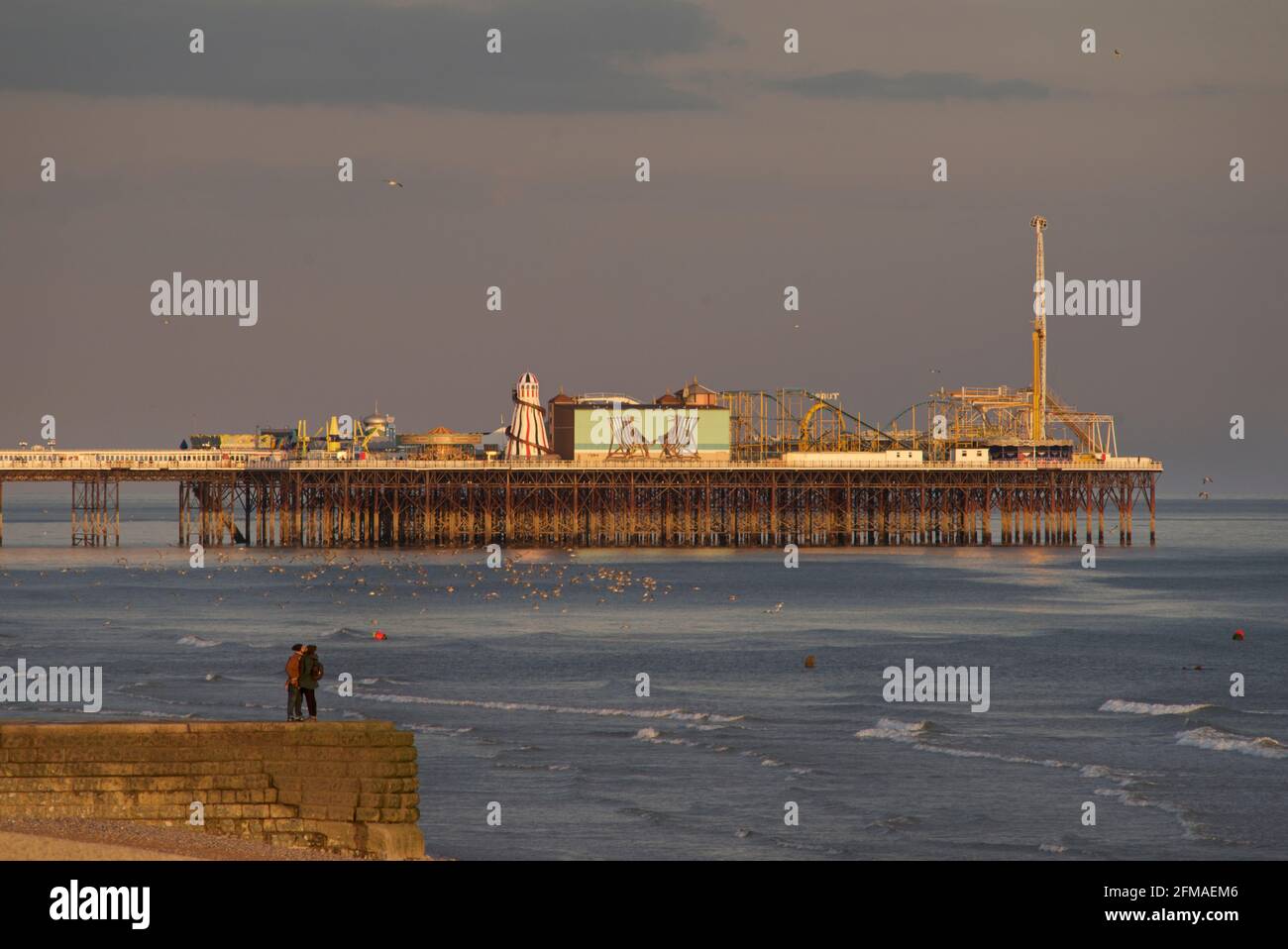 Pärchen n a groyne mit Brighton's Palace Pier im nachmittäglichen Glanz einer untergehenden Sonne. Brighton & Hove, Sussex, England, Großbritannien Stockfoto