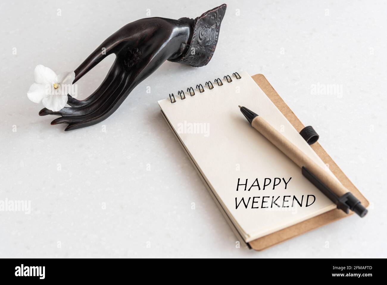 Happy Weekend Word in offenem Notizbuch und Blume in schwarzer Hand. Büroarbeitsplatz Stockfoto