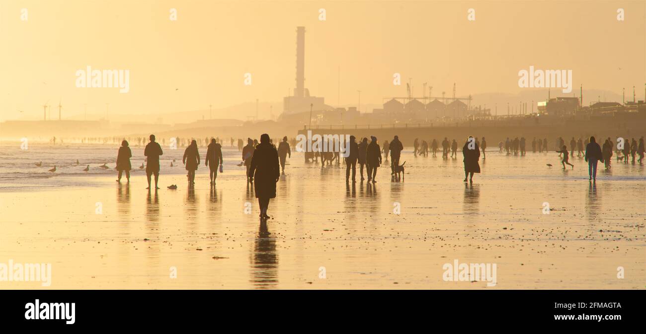 Brighton und Hove Beach bei Ebbe und Blick nach Westen. Silhouetten von Menschen, die bei Sonnenuntergang am Sandstrand entlang wandern. East Sussex, England. Remniscent eines Gemäldes von Lowry Stockfoto