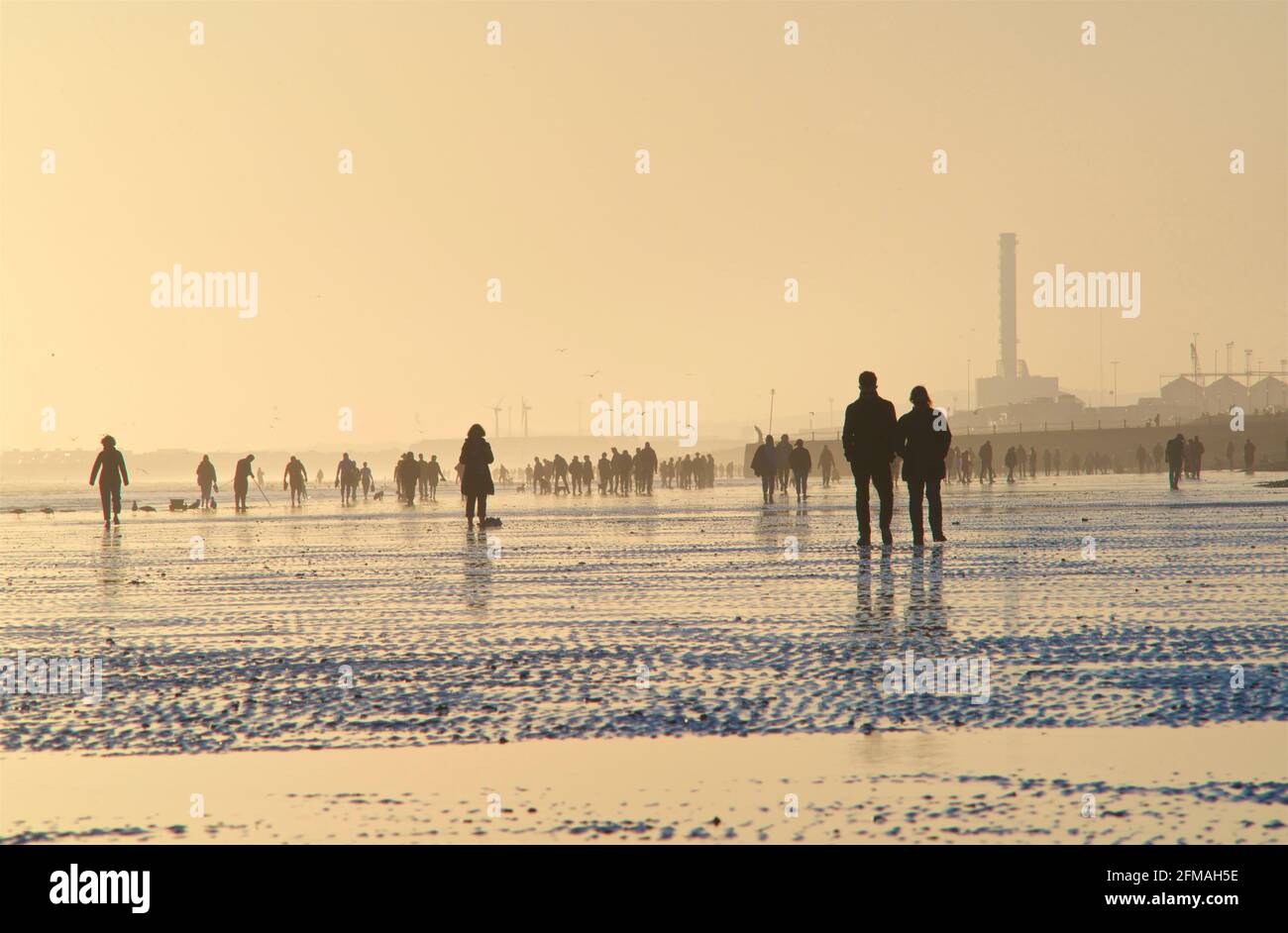 Brighton und Hove Beach bei Ebbe und Blick nach Westen. Silhouetten von Menschen, die bei Sonnenuntergang am Sandstrand entlang wandern. East Sussex, England. NEAP-Gezeiten Stockfoto