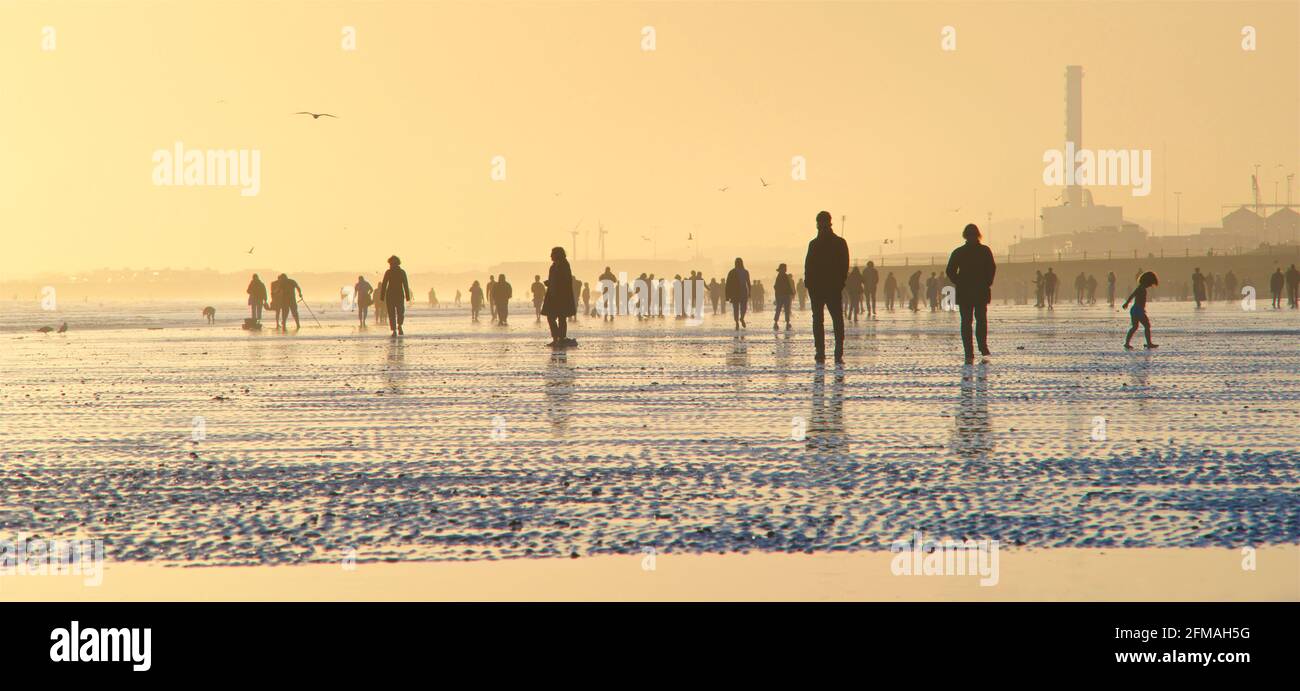 Brighton und Hove Beach bei Ebbe und Blick nach Westen. Silhouetten von Menschen, die bei Sonnenuntergang am Sandstrand entlang wandern. East Sussex, England. Remniscent eines Gemäldes von Lowry Stockfoto