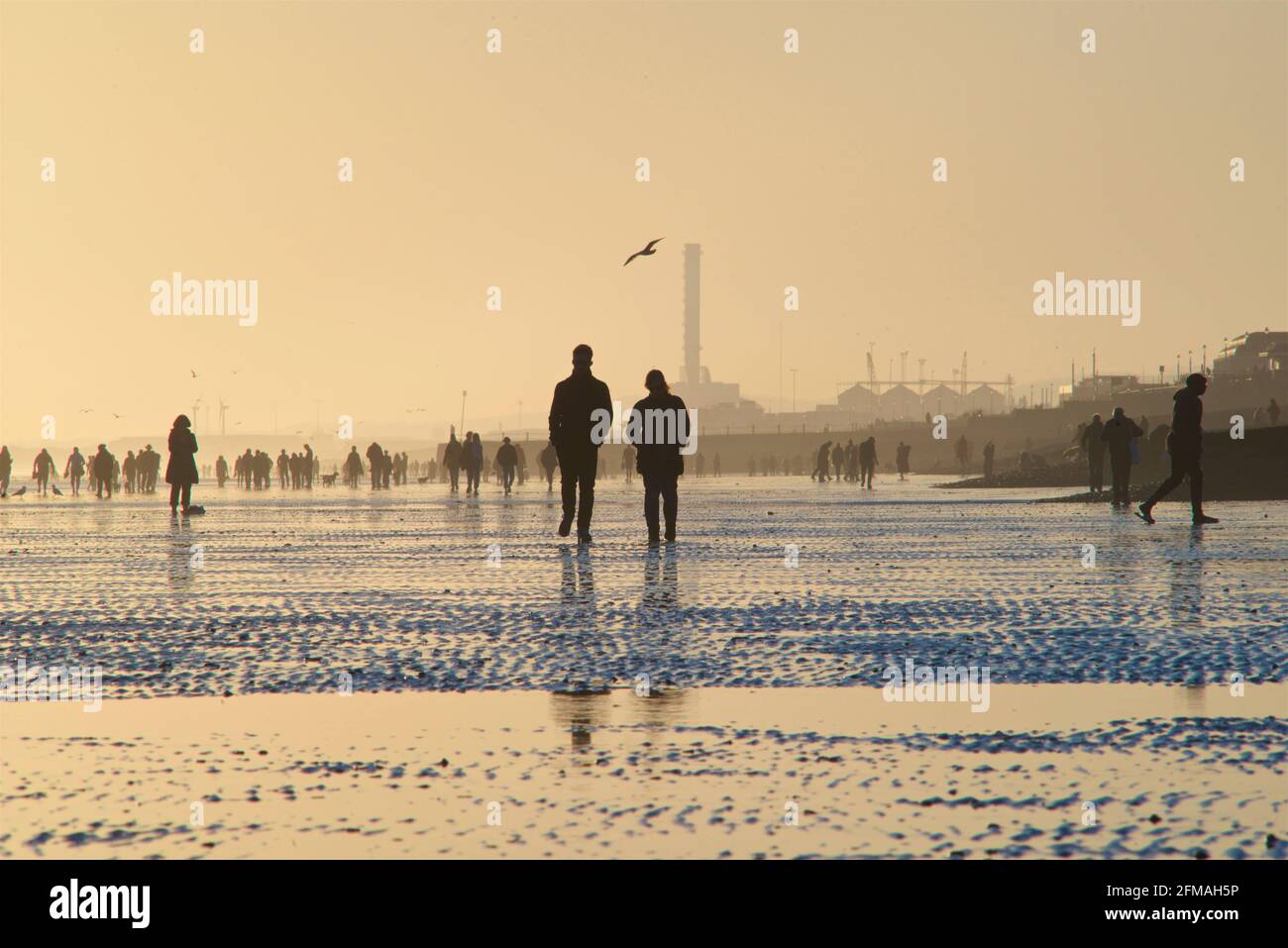 Brighton und Hove Beach bei Ebbe und Blick nach Westen. Silhouetten von Menschen, die bei Sonnenuntergang am Sandstrand entlang wandern. East Sussex, England. Remniscent eines Gemäldes von Lowry Stockfoto
