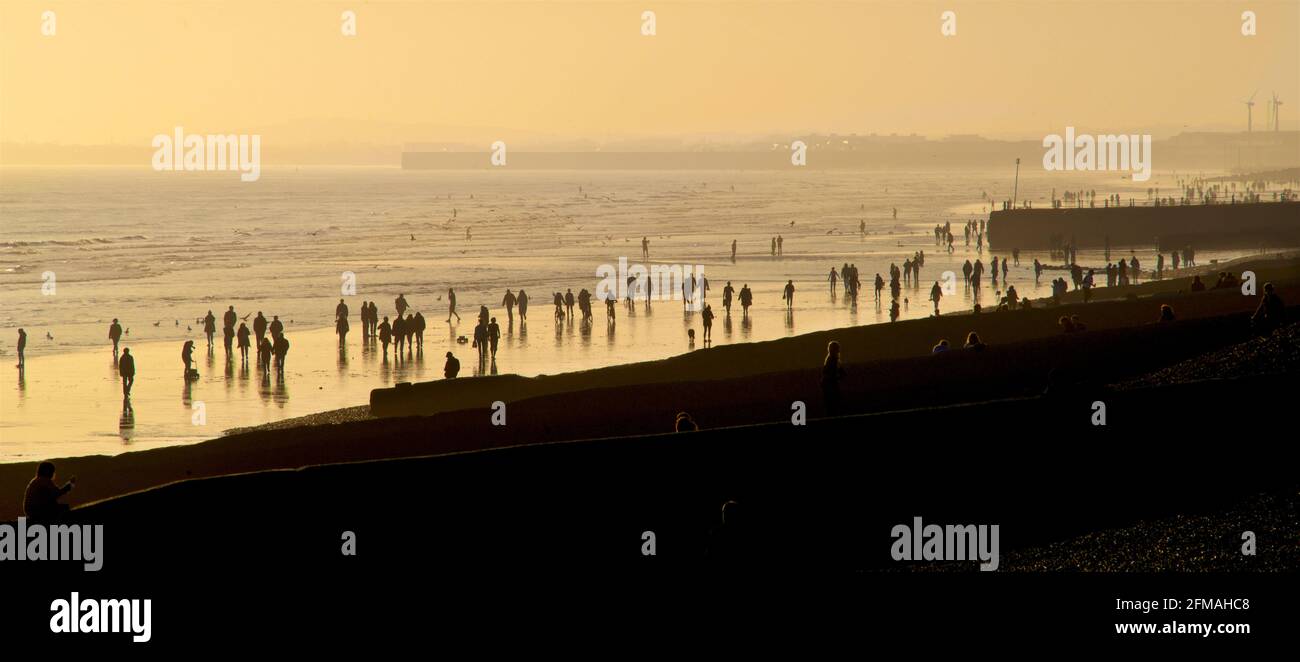 Brighton und Hove Beach bei Ebbe mit Blick nach Westen in Richtung Worthing. Silhouetten von Menschen, die bei Sonnenuntergang am Sandstrand entlang wandern. East Sussex, England Stockfoto
