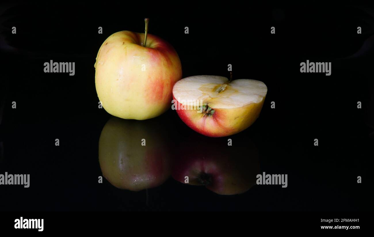 Essen Stillleben mit dem einen saftigen Apfel und die Hälfte Von der Frucht in einer Nahaufnahme auf einem Hochglanz Glatter schwarzer Hintergrund mit Früchten Spiegelreflexionen o Stockfoto