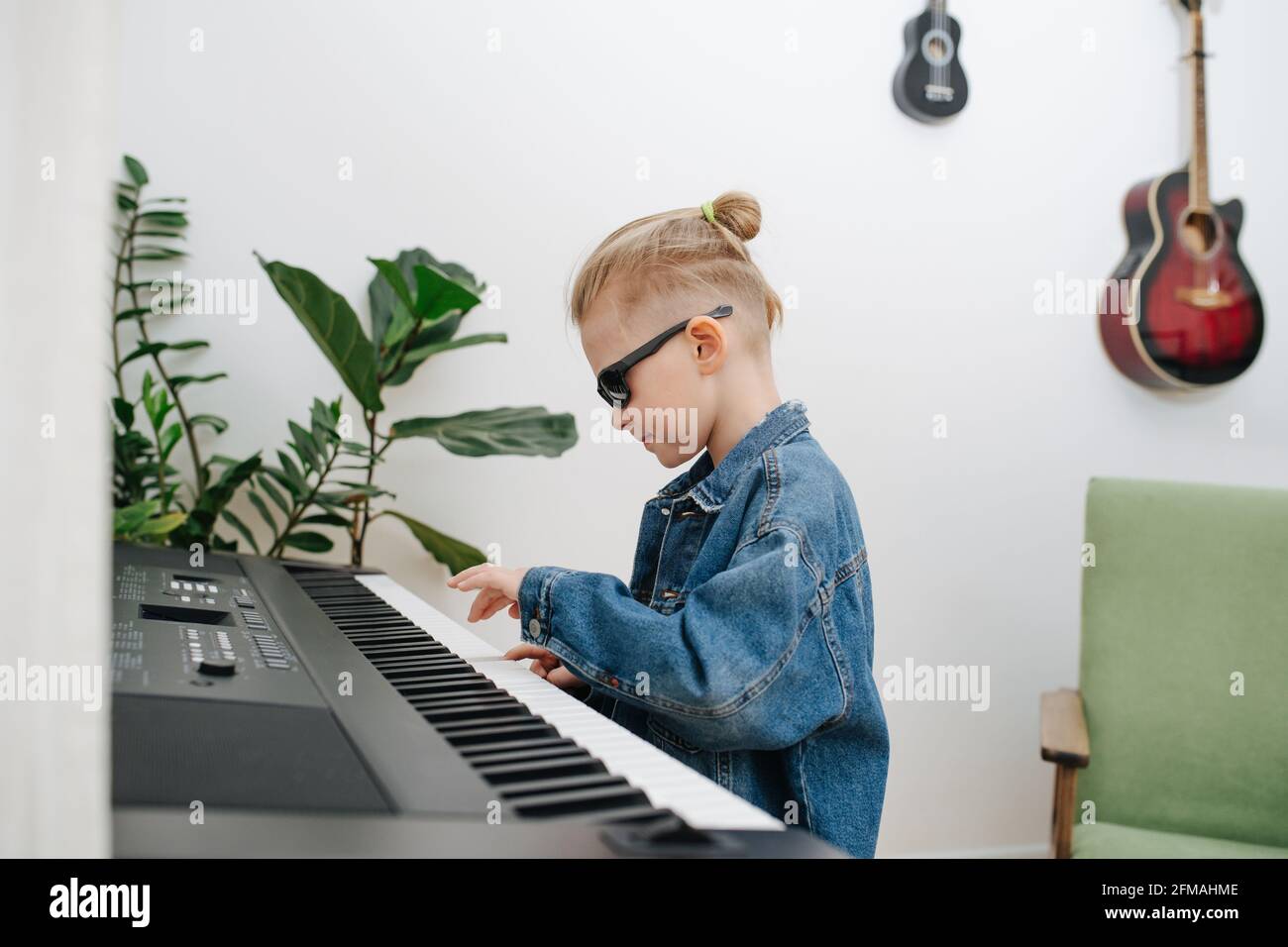 Der achtjährige Junge stellt sich vor, ein Musisier zu sein, während er zu Hause E-Piano spielt. Er trägt Jeans-Jacke und Sonnenbrille, h Stockfoto