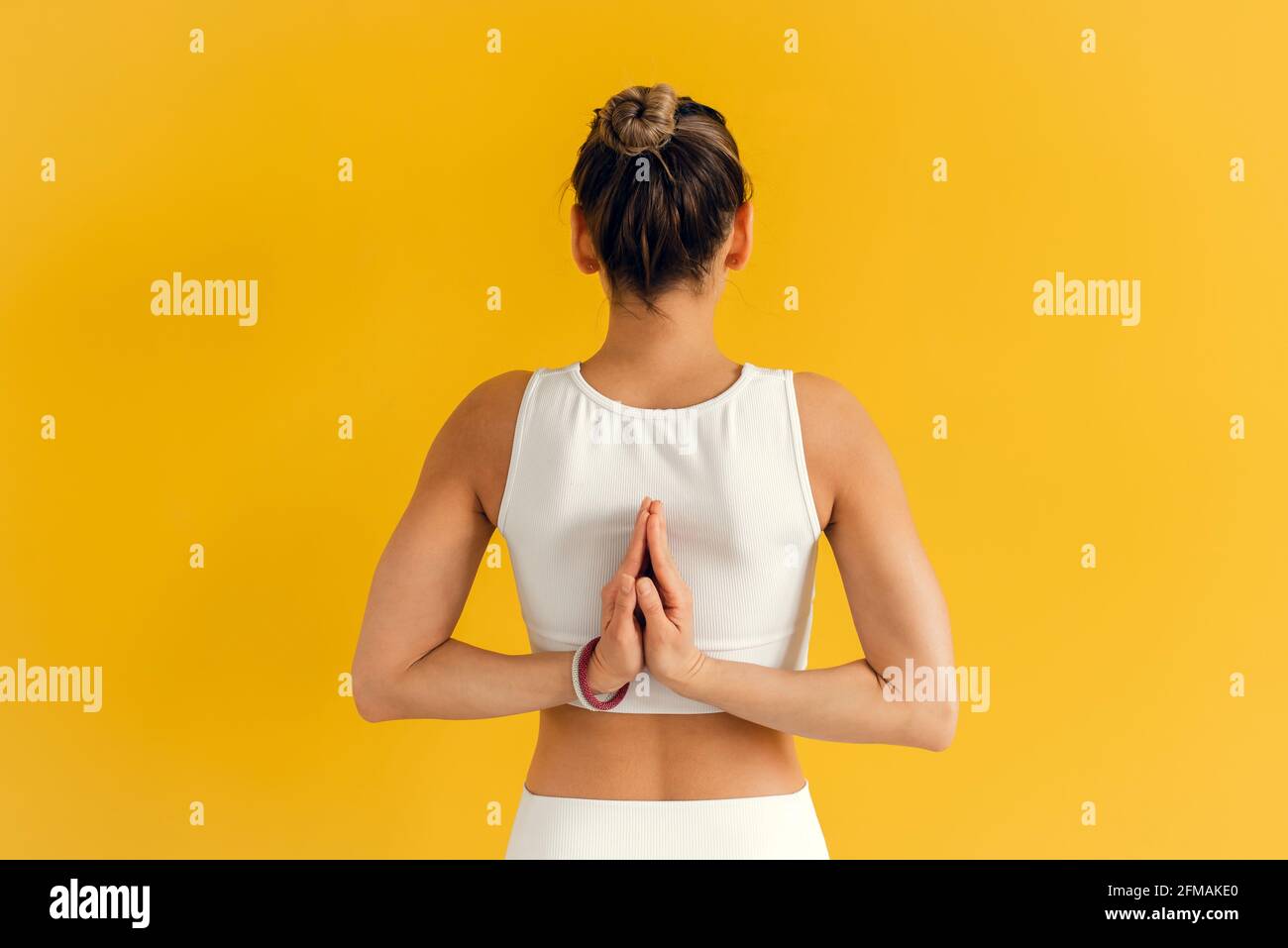 Nahaufnahme einer jungen Frau, die sich hinter ihrem Rücken die Hände anschließt, während sie Yoga-Übungen macht. Junge attraktive Yogi-Frau, die Yoga praktiziert und Namaste hinter sich lässt Stockfoto